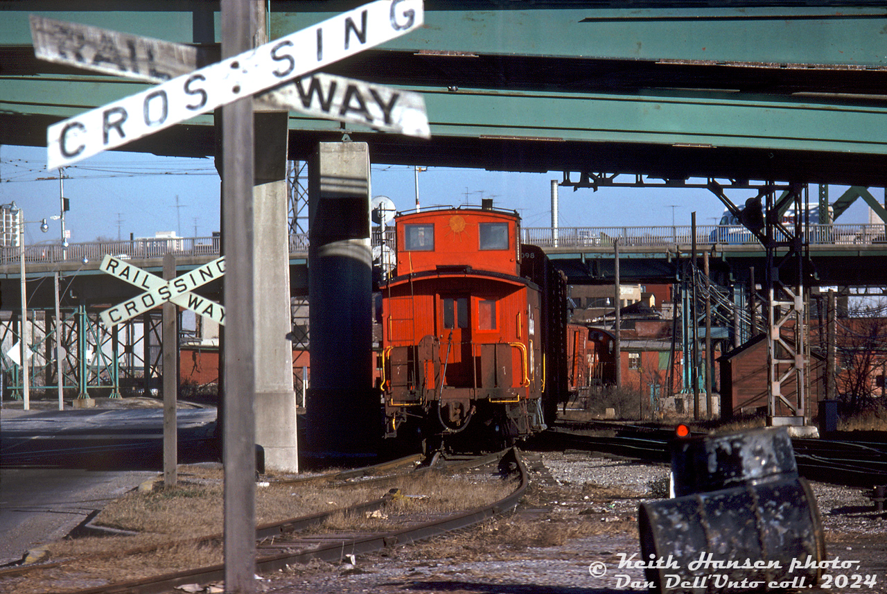 A wooden Canadian Pacific van (caboose) trails a short local freight job with a little Alco switcher in charge, pulling out of CP's Cherry Street yards and ducking under the Eastern Avenue and Queen Street overpasses as it crosses over CN's Bala Sub onto CP's Don Branch. The van had just cleared Bayview Avenue, and is equipped with a trainline-operated air whistle on the rear handrail for whistling during reverse movements over crossings.

A sun symbol on the cupola is an odd touch, according to "Nicholas Morant's Canadian Pacific", this was an old practice dating back many years when crews used to fasten ornaments to their assigned vans to personalize them and make it easier to pick theirs out of a lineup on the van track.

Since the steam era, CP had freight sheds and team track facilities in the Cherry Street area to the east of Union Station, specifically north of the rail corridor between the Don River and Cherry Street (with spurs and sidings continuing west). CP's Don Branch (Belleville Sub) was on the east side of CN's Bala Sub, so to access their own tracks CP would have to cross over CN first near Don. CP would also interchange cars here with CN at their own Cherry St. yards nearby.

In later years CP had a large freight shed here, but over time the largely industrial area fell into decline, and CP pulled up their Cherry Street industrial tracks around 1989-1991. The large shed would remain until most of the area was cleared out in the mid-2000's for a planned large-scale urban redevelopment of the formerly industrial West Donlands (today known as the Canary District).

Keith Hansen photo, Dan Dell'Unto collection slide.