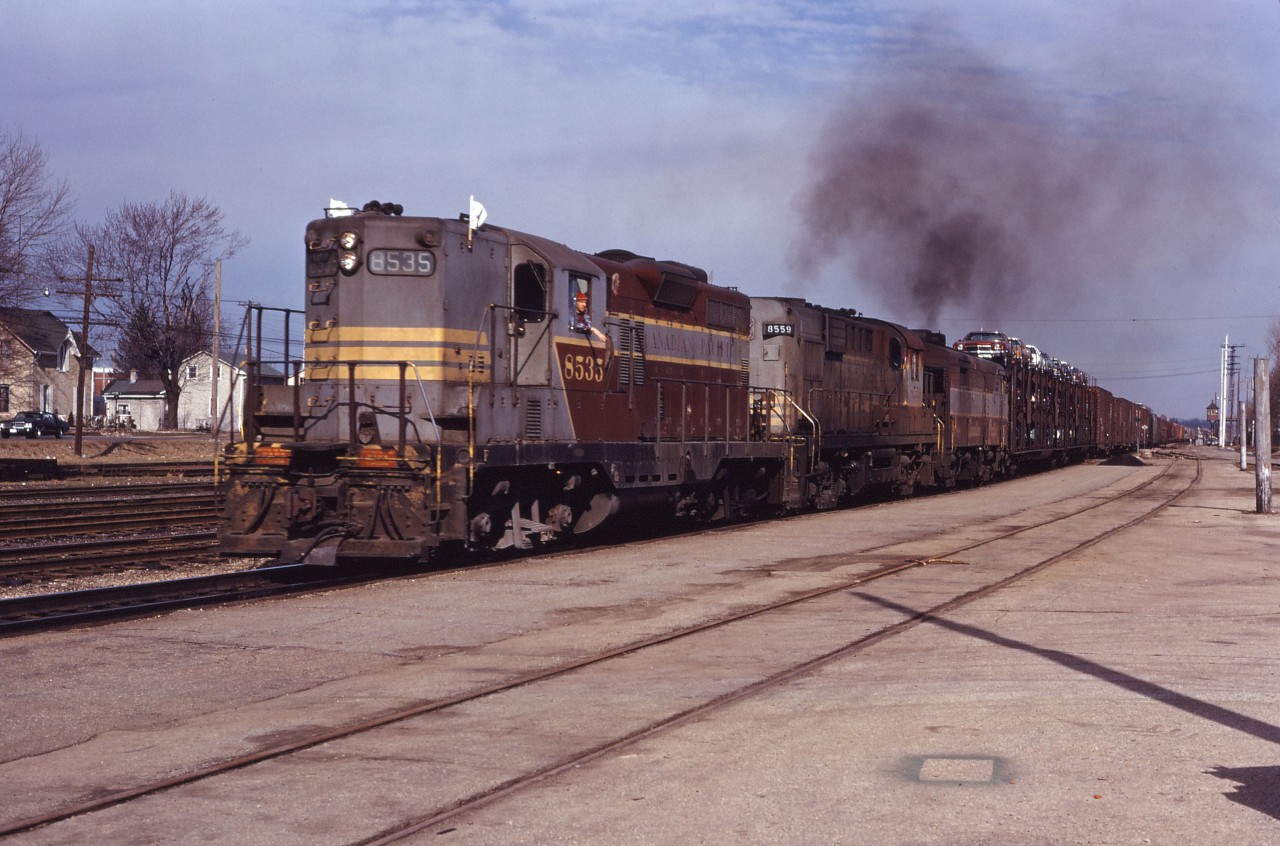 With lots of smoke, a CP westbound throttles up, taking "a run at the hill" to Orrs Lake. The train is still occupying the Dundas Street crossing (protected by a watchman in the distant tower) and will soon cross the Grand River as the operator at the Galt station--no doubt on the platform--inspects the train. Power is Western Lines GP9 8535, SGU-equipped RS10 8559, and an unidentified FPA2 or FA2. "OS Galt..."