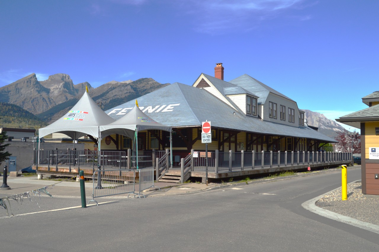 This image is just for the Station fans. Here is a summary regarding a station that went against (and survived) the usual fate of stations operated by the CP, a company known for its ruthless destruction of outdated structures all over the country since the late 1970s.
Fernie station was opened in 1909 and operated until 1964 when the last passenger train left town. The station eventually was donated to the city in 1979. In 1987, renovations started and a rather energetic effort had it finished and reopened in 1990. It featured all new but historically accurate windows. Because it had to be moved back from the tracks it also sits on a new solid concrete foundation.
It surfaced as a Community Arts and Crafts Centre.  And did well. The old baggage & freight area now supports live music and theatre. The ticket office area became a restaurant. Out front the platform is now a nice deck for train watching, and of course, having a few drinks.
Fernie prides itself in being a popular tourist stop and the station blends right in.
