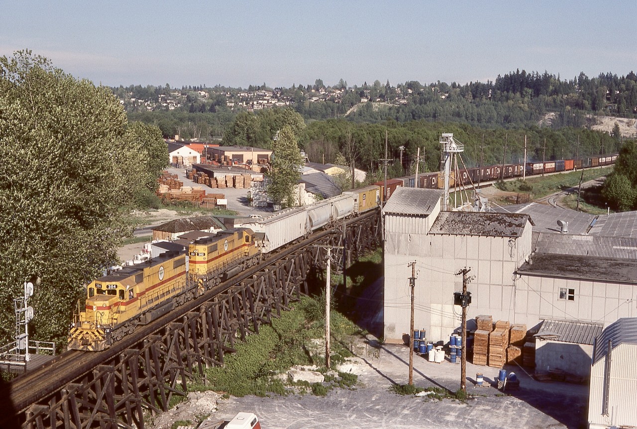 A pair of EMD SD38-2s, BC Hydro 384 and 382, brought a regular westward Valley Freight down Scott Hill and paused at the interlocking signal for the Fraser River Bridge to cross into New Westminster on Sunday 1982-05-09 at 1802 PDT, as seen here from the Patullo highway bridge sidewalk (ear plugs very handy for reducing road traffic noise).

This view was lucky timing for me, as twenty days later on 1982-05-26, a major fire involving the swing span of that Fraser River railway bridge completely disrupted local railway operations on BCH, CN, CP, VIA, and Amtrak, providing many photo opportunities when all rail traffic was detoured via a bridge from Mission City to Matsqui.
