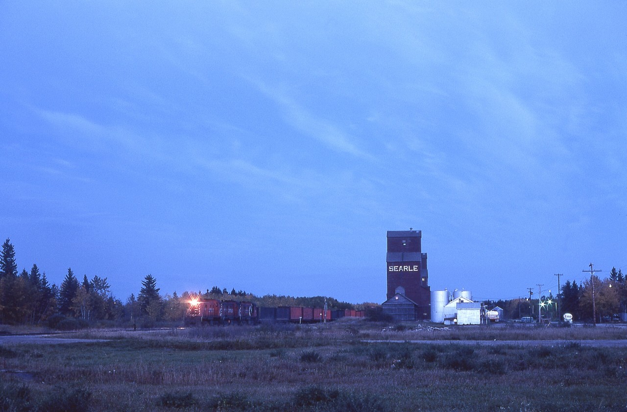 Westward and northward from Prince Albert, Canadian Pacific reached Meadow Lake via 60.3 miles of several joint trackage sections on Canadian National lines before reaching home road rails near Debden at Tobey, then continued through forested areas to Leoville.  Following that line via “interesting“ secondary roads one evening gained me this view of westward Meadow Lake train No. 97 with lightweight RS-23s CP 8018 + 8016 + 8014 in traditional elephant style (found to work best for radiator air flow) by the elevators at Leoville at 1925 CST, still with fifty-nine rail miles to go to reach Meadow Lake.