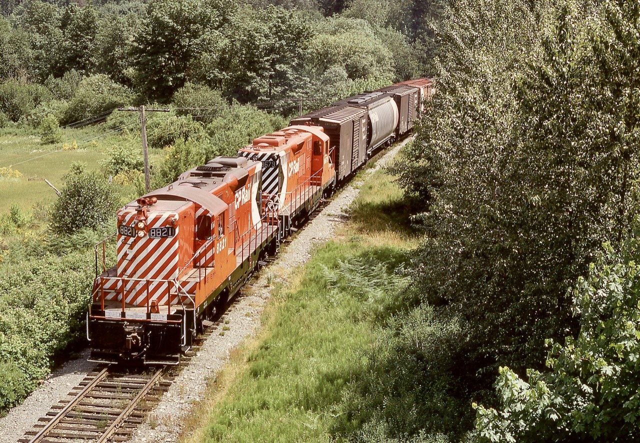 On Vancouver Island and from the era when clean locomotives were an everyday sight (and a great starter job for me), northward daily-except-Saturday freight train No. 51 from Victoria on Sunday 1972-06-11 had a pair of shiny GP9s, CP 8821 and 8679, as it approached the midway point in its journey to Stockett then as a yard movement on the spur to the yard and barge slip at Wellcox in Nanaimo.

Viewed from the Macmillan Bloedel log-haul truck road bridge paralleling CN’s Tidewater sub. bridge over the railway and TransCanada Highway at Koksilah, one detail that jumps out at me is the solid horizontal handrail on the front of 8821 where eventually a hinged crossover platform would be installed for secure movement of personnel between coupled units.