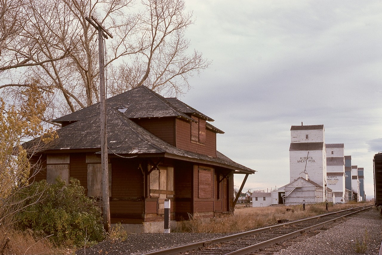 In 1974, on my first prairie-explorations road trip, CP’s Macleod subdivision was followed, and with no train encountered, depots were a primary camera target.  Cayley at mileage 47.9 (measured from 12th Street East in Calgary) had a boarded-up depot when seen on Tuesday 1974-10-15 looking southward, and that forecast the eventual closure of that subdivision from a junction at Aldersyde through to Fort Macleod, with the Aldersyde sub. from Aldersyde south to Coalhurst (now new Lethbridge for CPKC) as an alternate route.

Cayley was named for Hugh St. Quentin Cayley (1857-1934), member of the Council of the Northwest Territories from 1886 to 1896.  He was a Calgary newspaper publisher and later became a British Columbia judge.