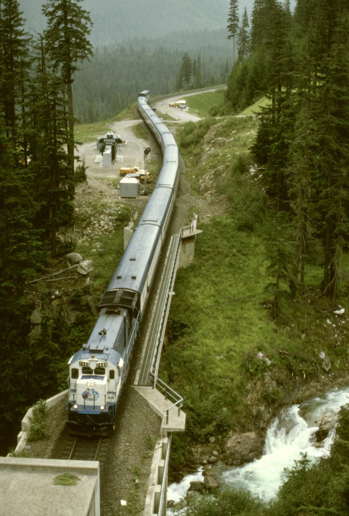 When CP closed the Connaught Tunnel in 1995 to deepen it to handle double-stacked containers, the normally westward-only Macdonald Track and Shaughnessy and Macdonald Tunnels had to accomodate all traffic, and to help maintain fluidity, a mechanical department troubleshooter was set up in an RV near Bear Creek between the two tunnels, meaning a paid-to-railfan vacation for me for a short while.

One reliable treat during daylight hours was the Rocky Mountaineer passenger train running under the original Great Canadian Railtour Company name, with two ex-AT&SF GE B36-7 units for power.  Here is an eastward passage, crossing Bear Creek at mileage 78.7 Macdonald Track at 1438 PDT on Monday 1995-07-31 with GCRC 7488 and twelve cars, and about to enter the Shaughnessy Tunnel.  The RV in the distance was my temporary home, and the facility on the left near the far end of the bridge was a transformer station plus backup generator for the rooftop jet fans in the tunnel.
