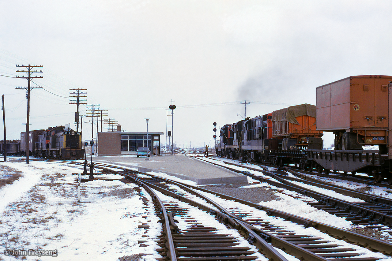 A pair of pups wait on the Uxbridge Subdivision for multiple trains to pass on the Oshawa Subdivision mainline, including this eastbound extra behind a GP9/RS18/H16-44 pairing.  The new Scarborough Junction station can be seen beyond the power, built in 1964 to replace the second station, which burnt down in 1960. This structure stood until the Midland Avenue grade separation project in 1977-78.

Scan and editing by Jacob Patterson.