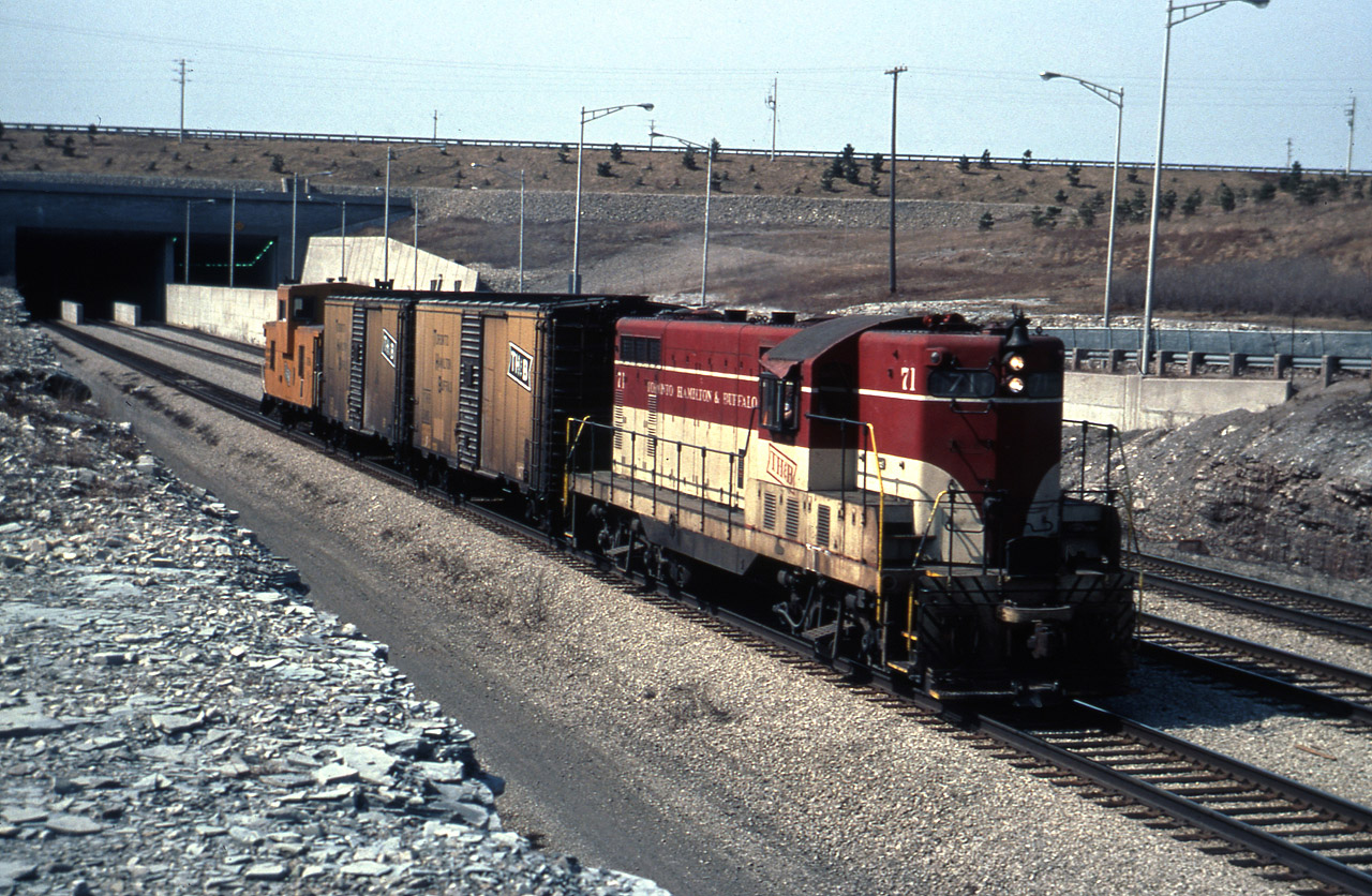 The original London GP-7 heading eastbound exiting the Townline Tunnel in an all TH&B consist, destination Port Colborne via the CNR Humberstone Sub.  The aptly named Townline Tunnel forms the municipal boundary between Welland and Port Colborne.  Most of the previous Welland Canal rail crossings (TH&B/NYC) in this area took place in central Welland between Broadway and Lincoln Streets.  #71 has less than a year to go before her tragic ending just west of here in Fenwick, ON - February 1980.  TH&B/CPR kept running rights into Port Colborne until 1988.  Today, on the Port Colborne side of the municipal town line (just south of where this photo is taken) is the site of one of the largest industrial projects in Canada, the $1.7B ASAHI KASEI Battery Separator materials plant.  Will it require rail service via the seldomly used Humberstone Spur ??  Time will tell.