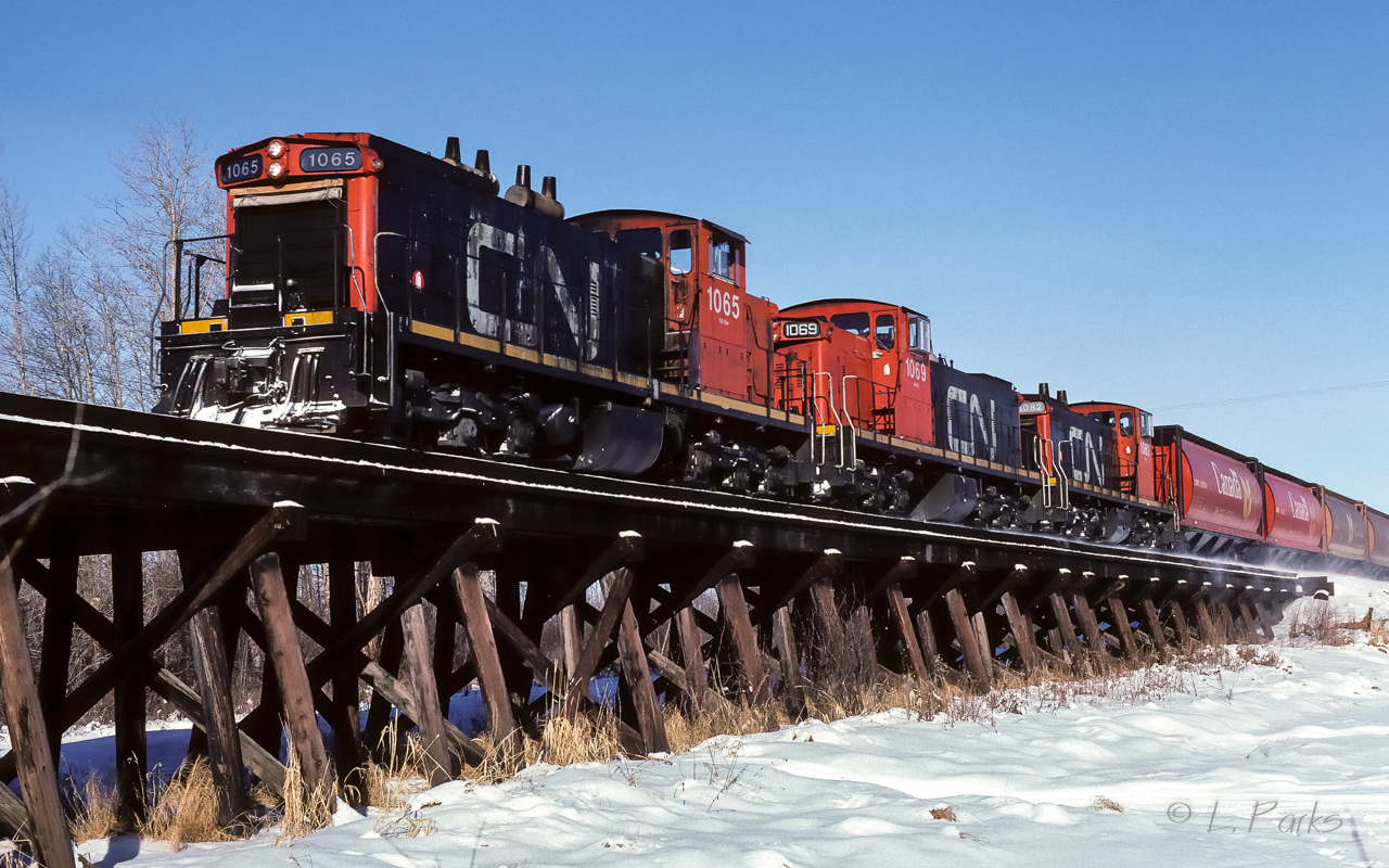 The snow dust swirling down by the hoppers shows the engineer has some speed on the train. As soon as the units have crossed the trestle, the hill up to Redwater starts. The grain extra has 31 loaded cars in tow and will pickup 3 more in Redwater, a nice sized train for these 3 units.