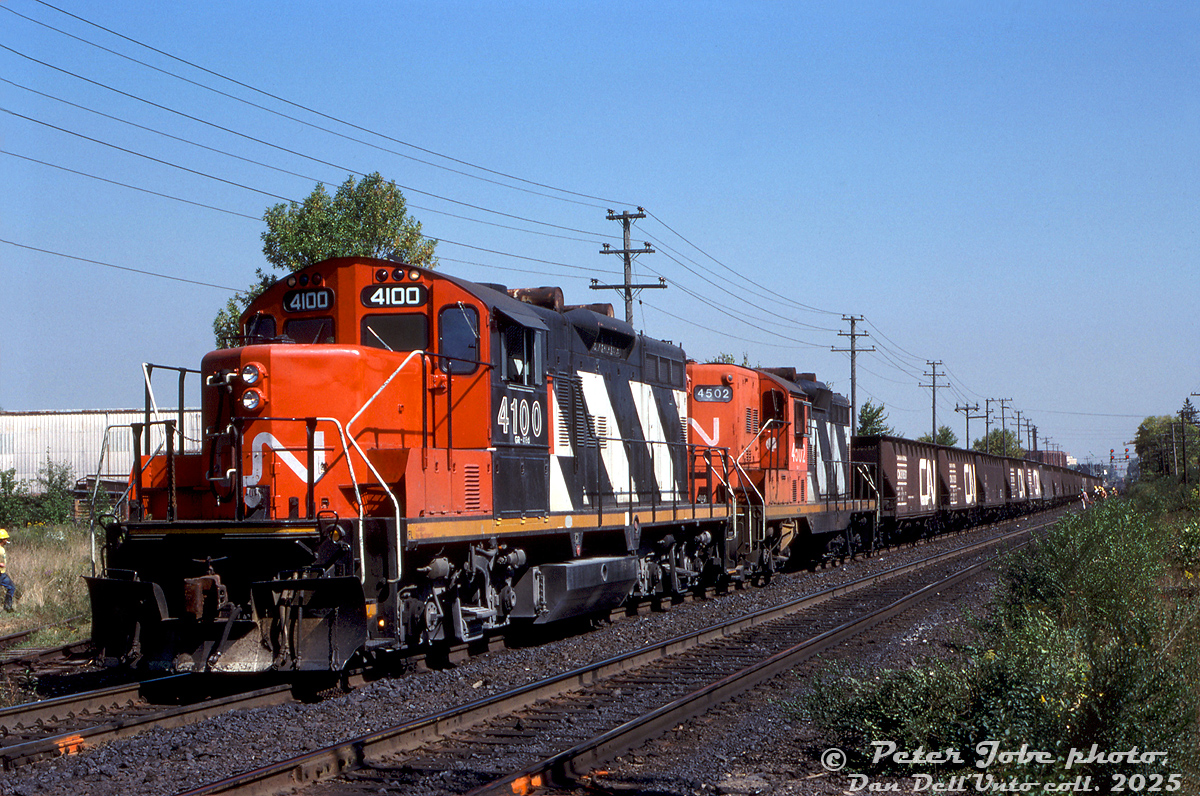 CN GP9RM 4100 and GP9 4502 work an extra work train dumping ballast on the Halton Sub, seen west of Brampton Station near Mile 16.0 with some CN track workers helping out. The downtown Brampton station is off in the distance, beyond the signals for the CN-CP Brampton diamond.

The switch on the left was for Moore Canada (dry kilns manufacturing), it's unclear when they closed down but the factory at Pleasantview & Fairglen was demolished sometime after 2002 for residential housing. Just behind the photographer was the switch for the Dixie Cup Spur at Mile 16.1. In 2007-2009, this section of the Halton Sub would get upgraded with a third track to the south, from Norval to just west of the diamond.

Peter Jobe photo, Dan Dell'Unto collection slide.