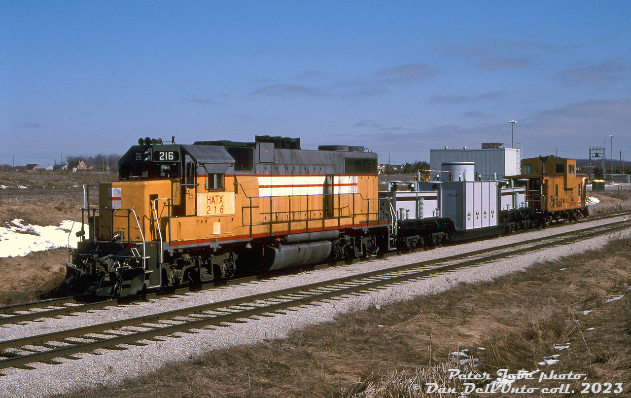 Unknown to most nearby, the special secretive nuclear train carrying radioactive uranium (spent fuel rods) from a nuclear power plant sits on an industrial siding near a quiet residential Brampton neighbourhood. This short train would almost cause a US-Canadian national emergency when hijackers commandeered another train full of Royal Canadian Mounted Police, and set it on a crash course towards this one, after leaving the nuclear plant. Disaster would be averted by the actions of a few courageous Mounties onboard.  Or so that was the plot of one episode of CBC's TV series "Due South" filmed in the mid-90's on CP's Owen Sound Sub in Brampton, Caledon and Orangeville. This was the nuclear prop train, featuring CP-leased HATX GP38-2 216 (an ex-UP/MP unit, now with HOG) back in the early-mid 90's when power-short CP was leasing anything it could get its paws on, an ancient 8-axle 309960-series heavy duty flatcar with a painted wooden nuclear waste prop load, and a caboose (likely for movements on the line, and not used for the scenes filmed). The train is shown parked on the spur tracks at the former Brampton Caterpillar assembly plant (opened 1983, closed in the early 90's due to an economic downturn and post-NAFTA plant consolidations) at Hurontario and Sandalwood in the Heart Lake area of Brampton. On this date, the "hero train" with the Mounties was also parked nearby. One story from a retired CP RTC dispatcher was that both movie trains were parked in Streetsville overnight after filming, and the crews stayed at local motels. Local residents complained to the Mississauga mayor's office about CP storing trains of nuclear waste in their area, and CP got a phone call about it. From then on the nuclear waste prop car was left out of town overnights, and tarped.  Peter Jobe photo, Dan Dell'Unto collection slide.