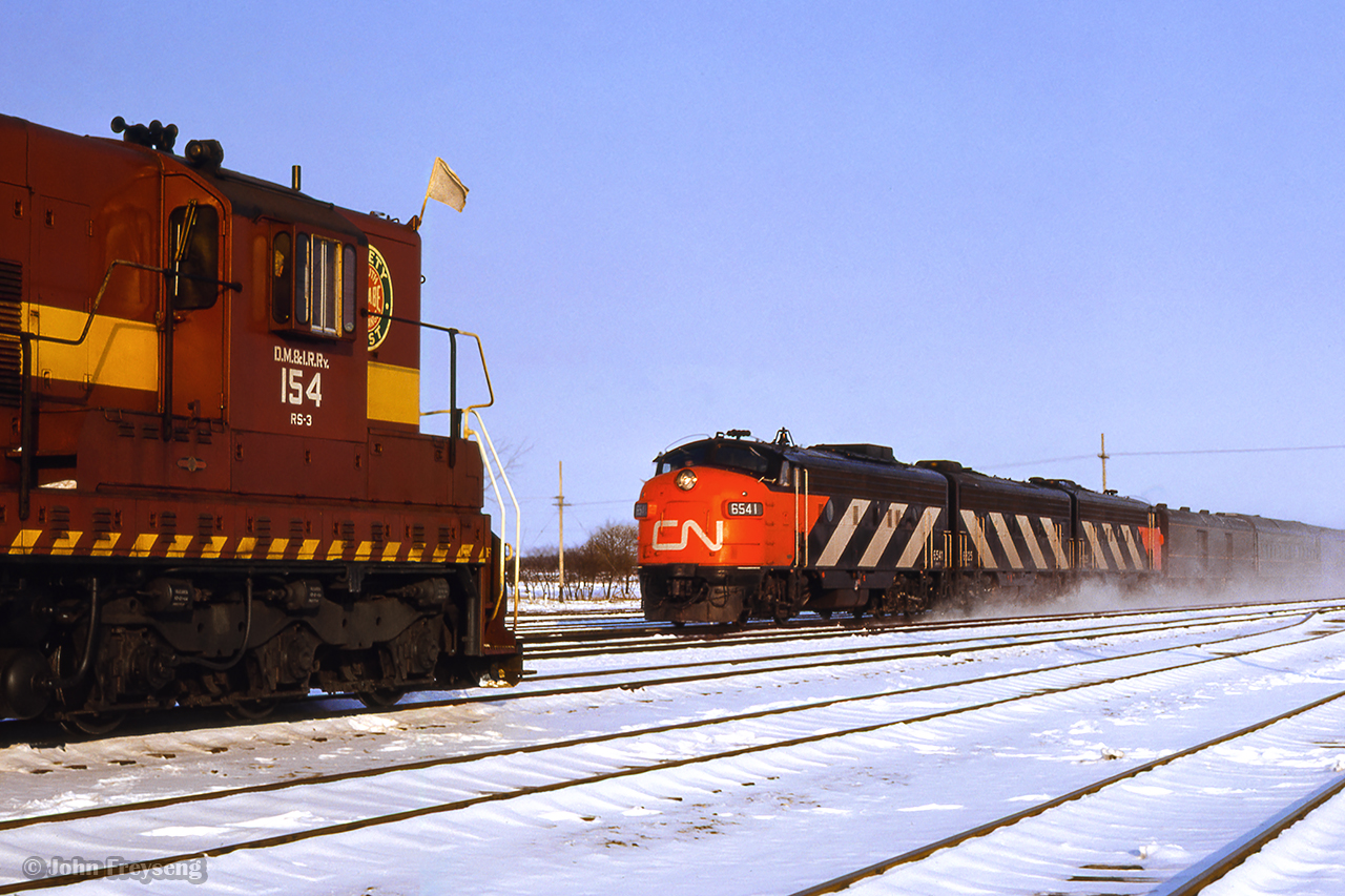 CN train 5, the Lakeshore, rolls into Belleville behind an A-B-A set of GMD FP9 units, passing Extra DMIR 154 east.  During the winters beginning 1963-1964 through the winter of 1973-1974, DM&IR SD9s and SD18s were often leased by CN, as well as CP and other lines, to fill out power shortages.  The winter of 1965/66 saw CN leasing 20 units.

Scan and editing by Jacob Patterson.