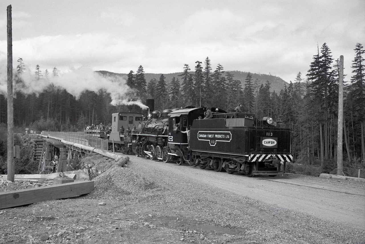 In early June throughout the 1970s, the Canadian Forest Products company town of Woss Camp (now plain Woss) on northern Vancouver Island hosted a Loggers’ Sports Day, open to the public, with the drawing card for railfans being passenger train excursions using CFP’s reserve steam locomotive 113 from Woss Camp to the Woss Lake reload and back, and that is how I got hooked on logging railway photography in 1971.  Here is that ALCo 2-8-2 built in August 1920 with a caboose and passenger flatcar returning across the Nimpkish River bridge into Woss Camp on Saturday 1975-06-07, successfully caught in an ideal rods-down position.
