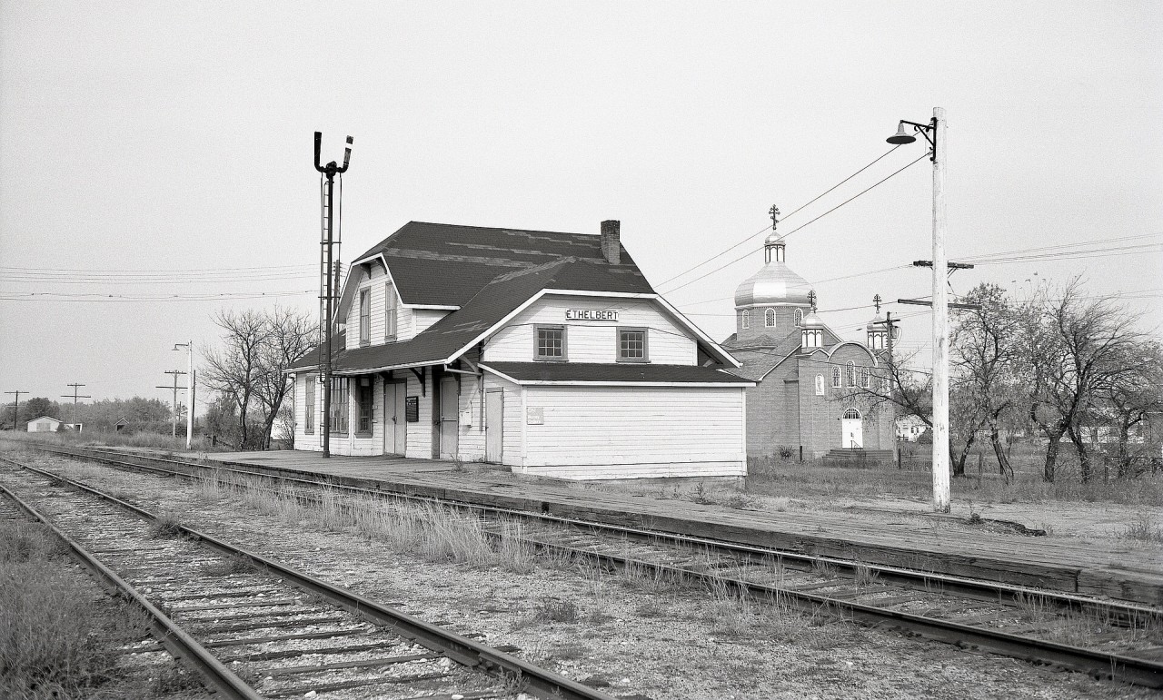 On CN’s Cowan subdivision between Dauphin and Swan River in Manitoba, there was a depot at Elthelbert at mileage 29.9, as built in 1898 by Canadian Northern Railway and shown here on Saturday 1976-10-02 looking northward.  That is the Sts. Peter and Paul Ukrainian Greek Othordox Church in the background, very handy many years later for me to determine the precise original location of that depot, which has been relocated to 27 km north of Winnipegosis to be a private residence.  To date, I have been unable to locate it on Google aerial views.

Ethelbert is reported as named for Ethel and Bertha, daughters of railway contractor William Mackenzie.