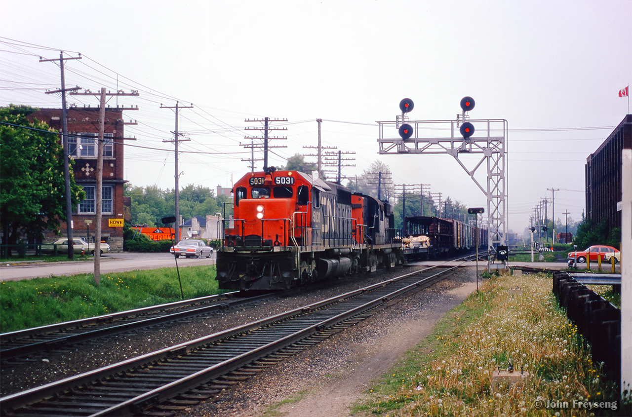 CN provides the entertainment while waiting on the arrival of CPR 1057 with an excursion from Orangeville.  Extra CN 5031 east pounds over the Brampton diamond the Mill Street crossing.

Scan and editing by Jacob Patterson.