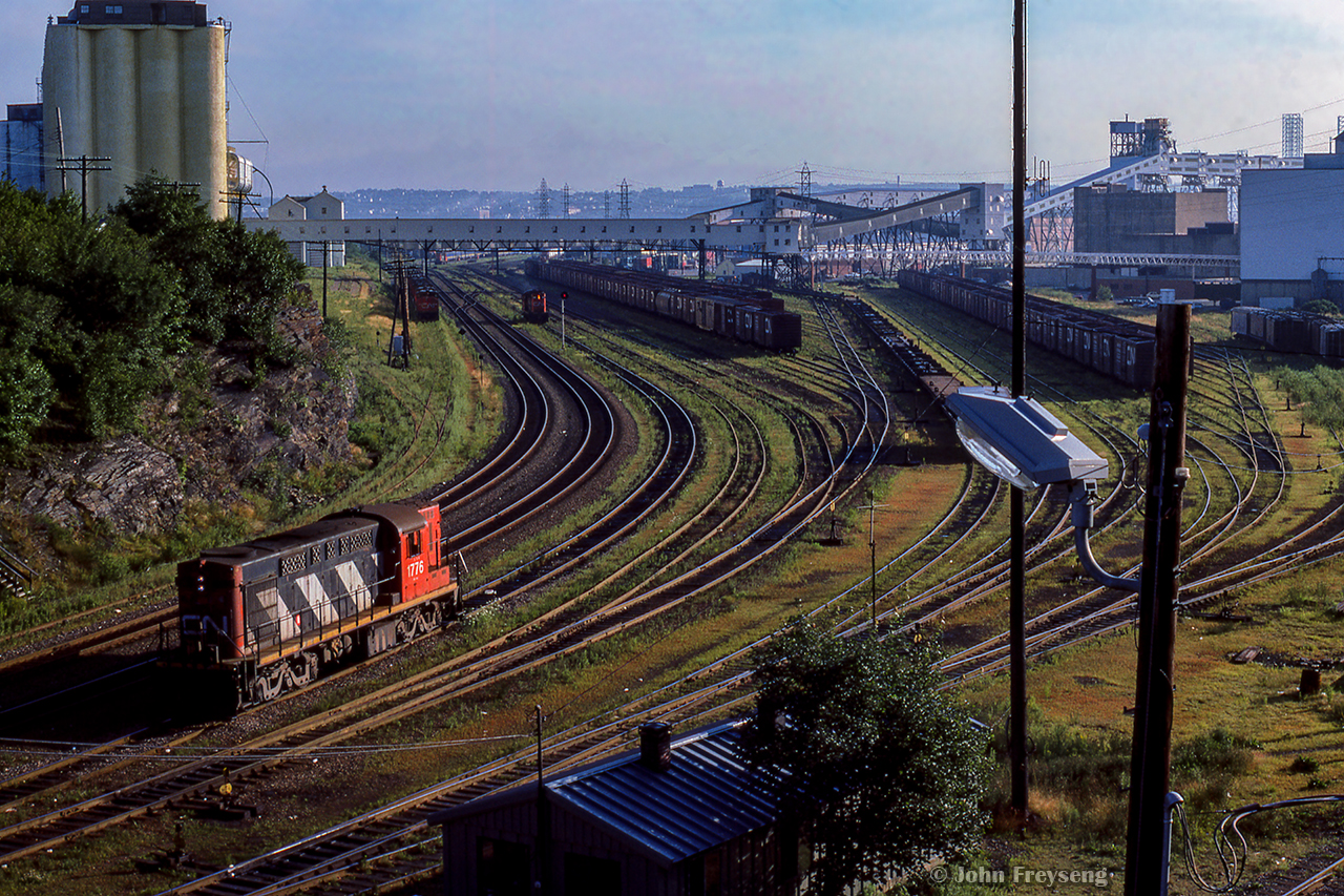 Looking east from the Young Avenue bridge, CN MLW RSC17 1776 sits in the Halifax yard, waiting for RS18 3660 in the distance to crawl up for a briefing between crews.  Both units will then begin switching their respective areas of the yard.  Note the string of locomotives at upper left, which may be in storage.

Scan and editing by Jacob Patterson.
