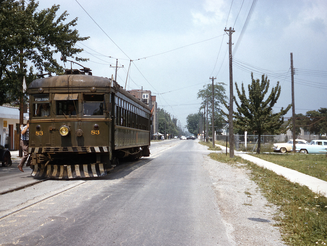 Flags a Flying....NS&T #83 south bound on Elm Street (Cranberry St.) at George Street in the Humberstone section of Port Colborne.  On the left is the former Humberstone Builders Supply (long since closed, now building demolished, soon to be housing), in the distance the Humberstone Shoe Company that dates from the early 1900's. The company was formed by German immigrant shoemakers that grew out of a small shop to over 400 employees at one point producing over 1,000,000 pairs of footwear per year.  At the end of production the factory had the contract with the Canadian Armed Forces for military boots, and made steel toed boots for commercial / industrial markets as well.  The plant was converted to apartments in the 1990's.   The ballpark on the right still exists on land donated by the Humberstone Shoe Company, and is aptly named Humberstone Shoe Park.