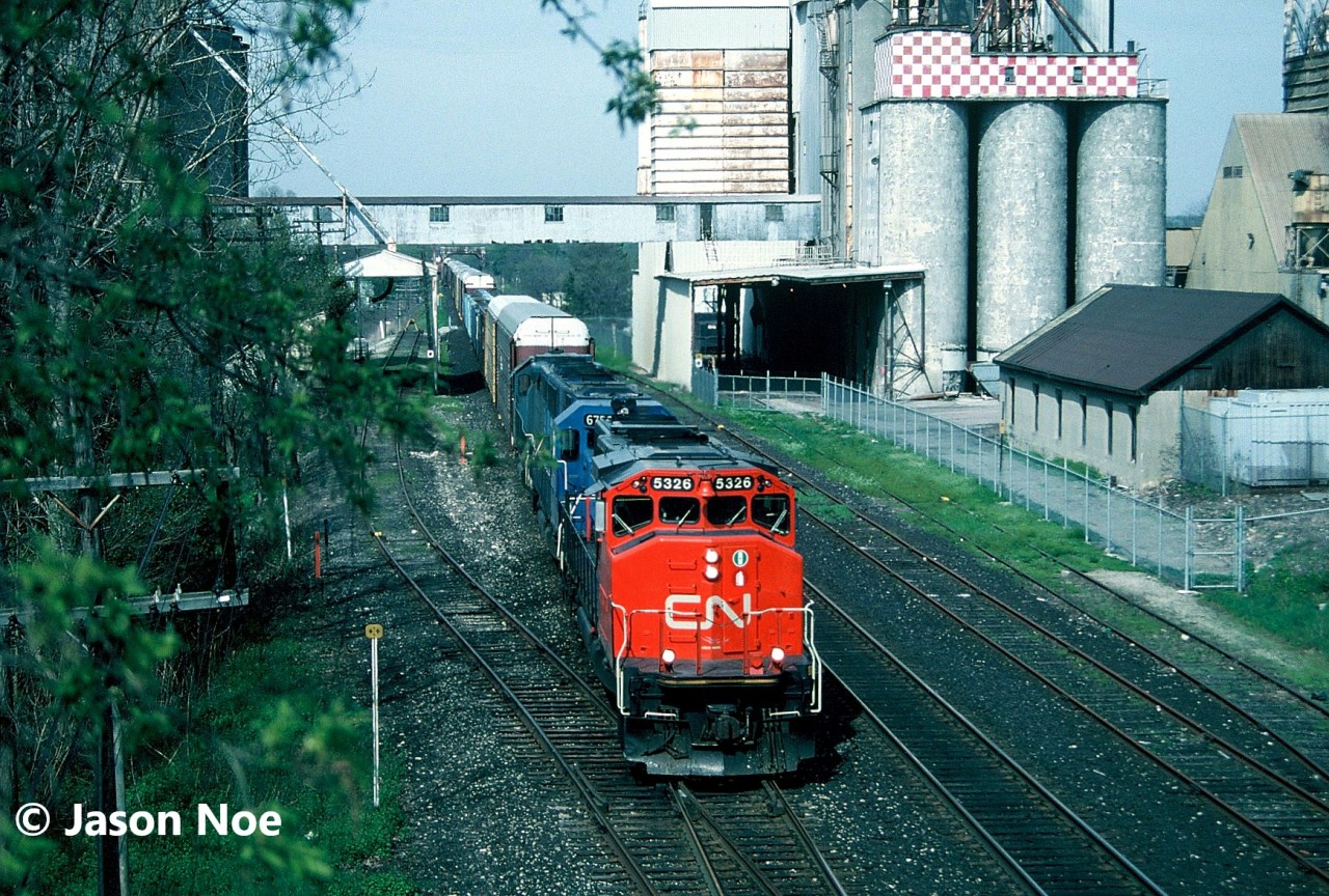 CN 392 with SD40-2(W) 5326, Conrail SD50 6753 and EMD Leasing GP38-2 763 are pictured heading east through Woodstock, Ontario on the Dundas Subdivision.  Conrail 6753 was either running through or operating on CN to repay back horsepower hours owed.  The train was passing under the large Purina Canada mill, which eventually under the Cargill empire had ceased operations during 2024.