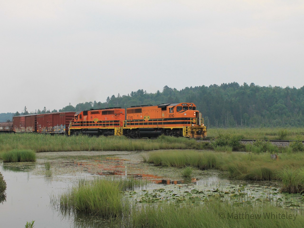 Under a wildfire haze filled sky, Huron Central train 913 is seen passing through a swamp near Whitefish with 20 cars bound for Sault Ste. Marie in tow. Power on this trip was HCRY 3010 and RLK 3409.


Just out of frame to the left lies the Crean Hill Mine's spur roadbed, which once connected to the Webbwood Sub at this location. While the tracks have long been removed, a small wooden bridge remains and appears to now be in use as an access road along with the remaining ballast path.