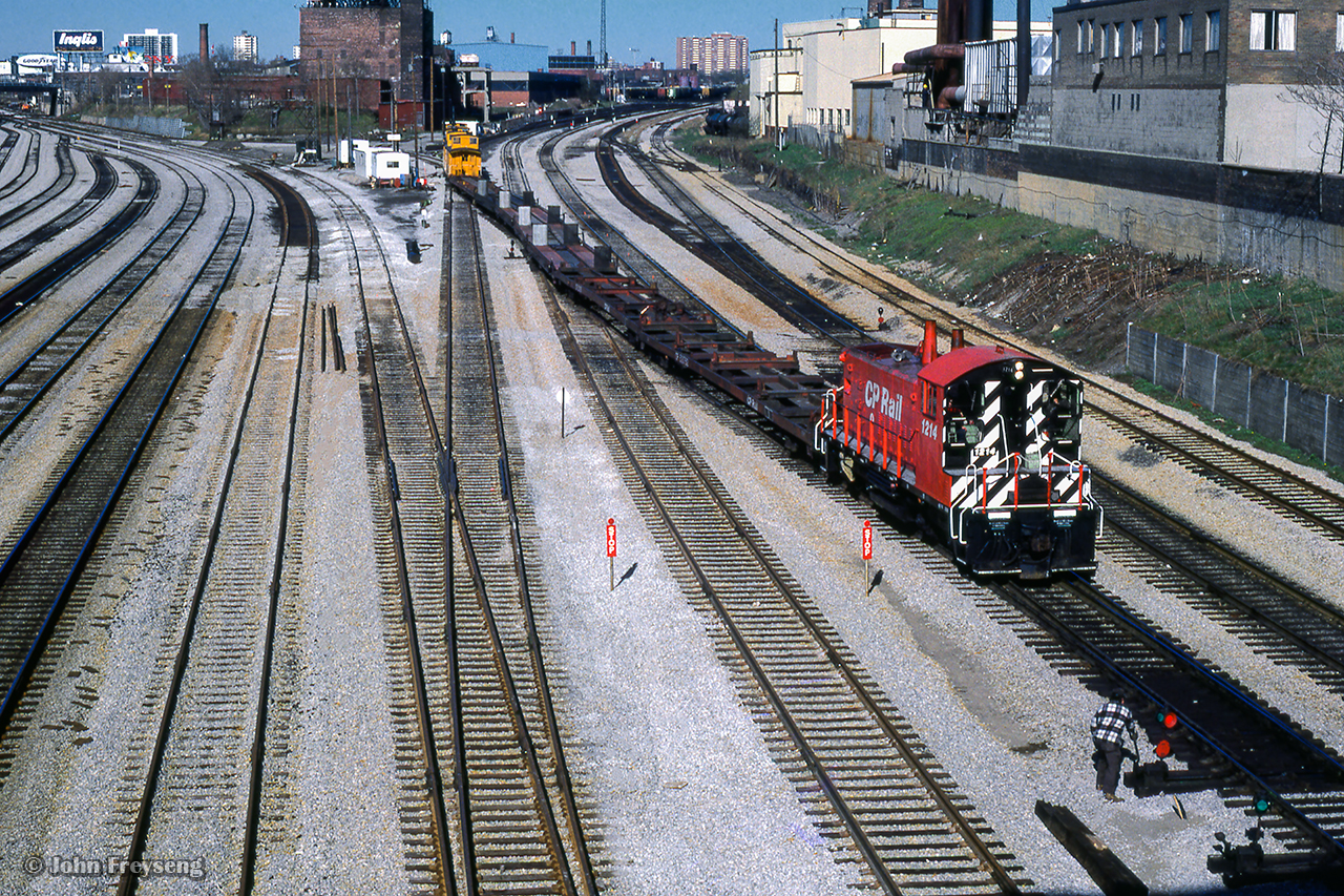 The switch ahead of 1214 is reversed allowing the SW1200RSu and train of TOFC flats to proceed through the former Cabin D area to downtown TOFC ramps.  Five wooden vans bring up the rear of the movement.

Scan and editing by Jacob Patterson.
