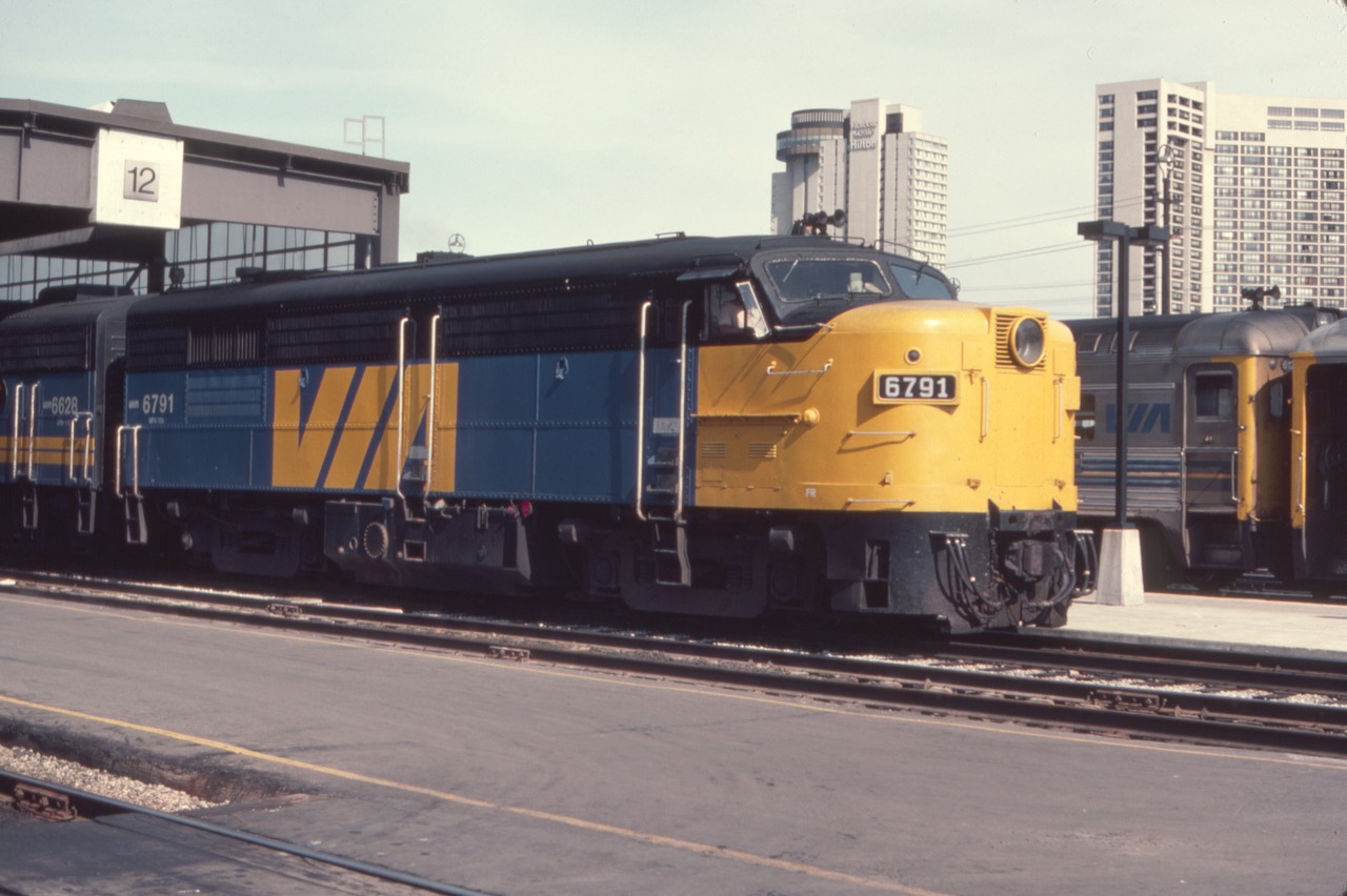 Via MLW FPA4 6791 is on the head end of a westbound passenger train ready to leave Toronto Union Station in August of 1982. The juxtaposition of the elderly "Alco" with the Harbor Castle Hilton tower (seen above the locomotive), complete with rooftop revolving restaurant, is interesting to me.