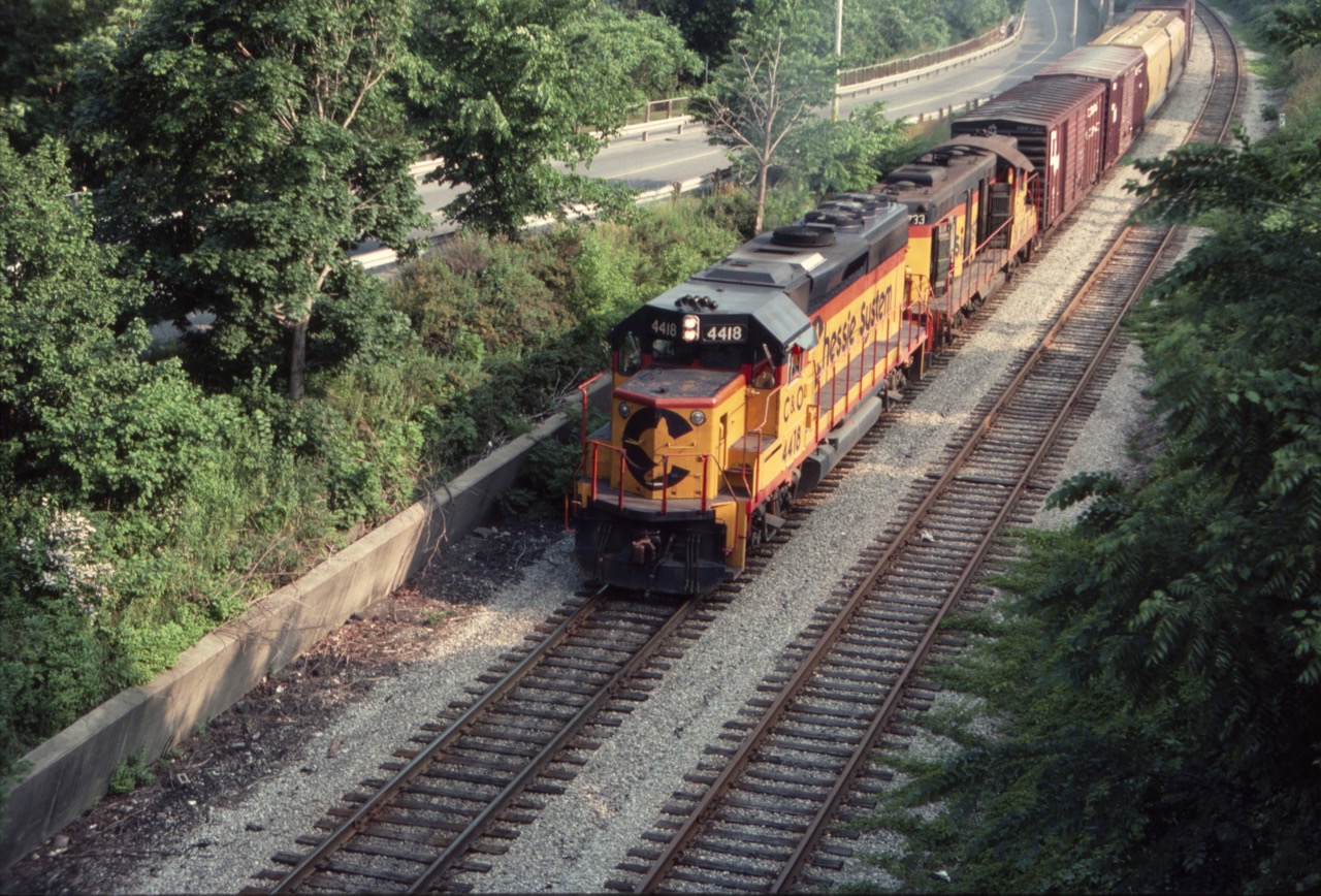 EMD locomotive C&O 4418 leads a Buffalo-bound Chessie freight along Portage Road towards Clifton Hill in Niagara Falls. Shortly thereafter it will cross the Michigan Central bridge to the USA, on a hot summer day in July of 1983. The high-nose geep behind the 4418 has lots of doors open, perhaps locomotive issues enroute across Ontario? Imagine my surprise coming back to this same location in 2004 and finding the two tracks ripped up, and new hotels and a casino built up. The beautiful Canadian Horseshoe Falls are just a stone's throw down the hill.