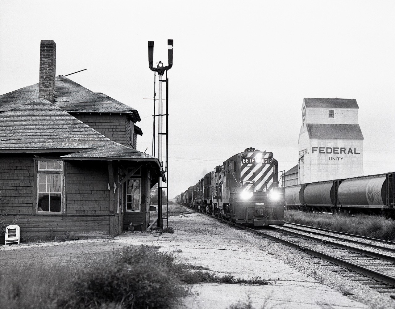 While not as busy as CN’s Wainwright subdivision mainline nearby to the south, CP’s Hardisty subdivision through Unity, SK, had the advantage of a staffed train order office, seen here with a CLEAR board for scheduled westward freight No. 561 with GP9 8618 leading C-425s 4214 and 4215 and GP9 8648 on Sunday 1981-09-27 at 1843 CST.

That depot is a survivor, now part of the nearby Unity & District Heritage Museum at GPS 52.4487, -109.1479 near 1st Street East and Main Street.
