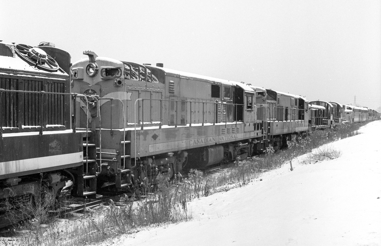 It is a cloudy November 30, 1968 in London, Ontario. At the CN Reclamation Yard, CLC road switchers, ALCO or MLW road switchers, and CLC C-Liners are visible. Some seem to be complete locomotives while others are just rusting hulks.