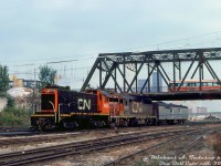 There's something at Bathurst Street for everyone to like: CN S13 8515 switches the head end of a passenger train at Cabin D, below the Bathurst Street bridge at the TTR's "Cabin D" interlocking. Well-worn CN GP40 4017, one of two GP40's with high-speed gearing assigned to corridor passenger service out of Spadina Roundhouse, trails with a 15300-series Tempo generator baggage (one of three converted from baggage cars with a HEP unit for use with Tempo trains). Above, nearly new TTC CLRV 4014 rolls south over Bathurst Street bridge on a southbound 511 Bathurst run.<br><br>Changes are underway in the background with construction of the flyunder, and reconstruction of Bathurst North Yard for GO layover use (the interlocking here would be renamed "Bathurst Street" when Cabin D was closed in 1983 and replaced by an automated interlocking plant controlled remotely from TTR John St. interlocking tower. That CN yard tower visible would also be demolished). Also of note in this scene is the Bathurst Tool building at Front & Bathurst, and in the background traces of the downtown Toronto skyline (also, check out all the tell-tails hanging down above the track!).<br><br><i>Michael A. Tedesco photo, Dan Dell'Unto collection slide.</i>