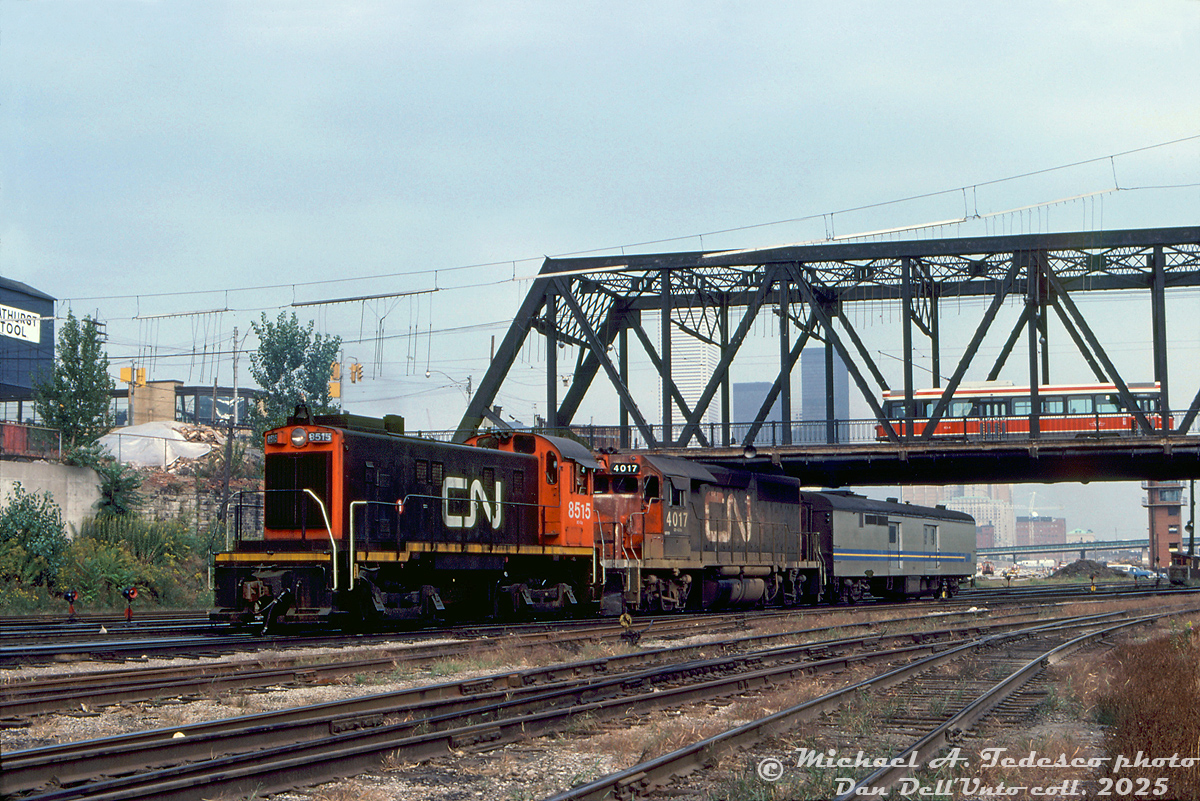 There's something at Bathurst Street for everyone to like: CN S13 8515 switches the head end of a passenger train at Cabin D, below the Bathurst Street bridge at the TTR's "Cabin D" interlocking. Well-worn CN GP40 4017, one of two GP40's with high-speed gearing assigned to corridor passenger service out of Spadina Roundhouse, trails with a 15300-series Tempo generator baggage (one of three converted from baggage cars with a HEP unit for use with Tempo trains). Above, nearly new TTC CLRV 4014 rolls south over Bathurst Street bridge on a southbound 511 Bathurst run.

Changes are underway in the background with construction of the flyunder, and reconstruction of Bathurst North Yard for GO layover use (the interlocking here would be renamed "Bathurst Street" when Cabin D was closed in 1983 and replaced by an automated interlocking plant controlled remotely from TTR John St. interlocking tower. That CN yard tower visible would also be demolished). Also of note in this scene is the Bathurst Tool building at Front & Bathurst, and in the background traces of the downtown Toronto skyline.

Michael A. Tedesco photo, Dan Dell'Unto collection slide.