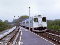 A 4-pack of GO Transit self-powered single level cars, lead by D704, arrive eastbound at Long Branch GO station in Toronto's west end. The consist is bound for Union Station downtown, and ultimately Pickering GO Station at the other end of the Lakeshore line. Some people linger on the tracks in groups past the bridge, possibly railfans on an unknown fantrip or outing trackside.<br><br>Along with all the single-level RTC-85 commuter cars GO purchased from Hawker Siddeley Canada for their startup in 1967 (and subsequent expansions), GO purchased nine self-powered versions, dubbed RTC-85SP (and RTC-85SPD for two units with dual cabs). They were intended to provide off-peak service on the Lakeshore line. Due to reliability issues, they were depowered and turned into cab cars in the mid-70's.<br><br><i>Original photographer unknown, Dan Dell'Unto collection slide.</i>
