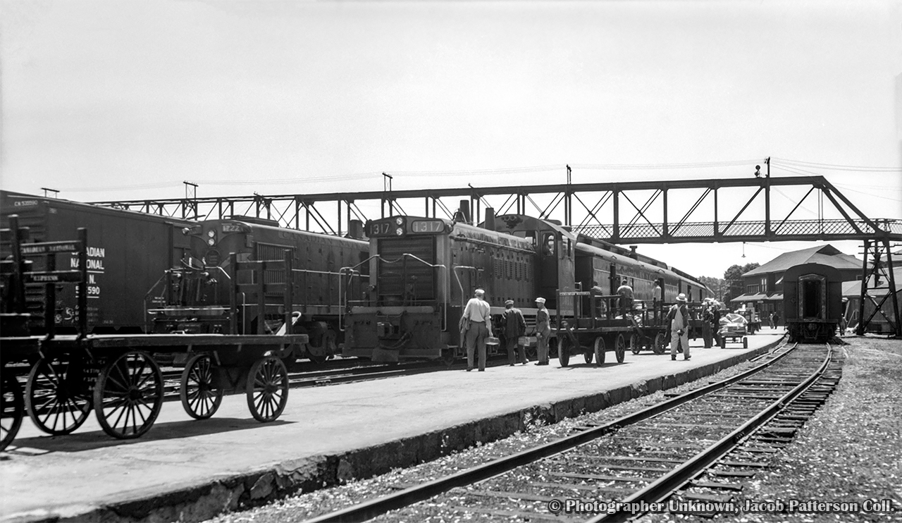 Pausing at Palmerston, brand new GMD SW1200RS 1317, built in August 1958, is in charge of Hamilton - Owen Sound train 173.  Diesel locomotives have only appeared in Palmerston during the previous two years, and primarily MLW RSC13s, such as 1722 at left on the point of mixed train M329 for Southampton.  

During this short stop, crew members are busy handling mail and express shipments into the RPO and baggage cars, while an outbound crew, potentially that of M329 at left, take in the sight of the new locomotive.  At right, the coach for mixed train M331 to Kincardine is spotted on the stub track.  After 173's 1120h departure, both M331 and M329 will depart at 1135h. The mixed trains will arrive back at Palmerston at 1525h and 1530h respectively, giving passengers half an hour until the 1600h arrival of 174 for Hamilton.

Original Photographer Unknown, Jacob Patterson Collection Negative.