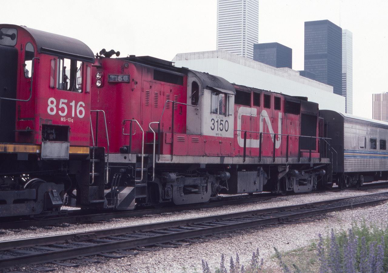 This view from July of 1982 shows CN 8516 shoving a Via westbound train towards the Toronto Union Station Train shed from the coach yards. It's great to see the CN 3150 in service, a MLW RS-18 modified for Tempo trains.  The Toronto skyline is prominent in the background, including the big white Bank of Montreal skyscraper.