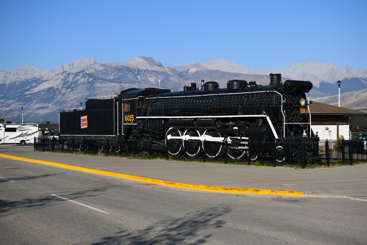 Majestic  
Background or foreground, take your pick. Both the mountains and the locomotive are majestic in their own right. 
CN 6015 continues to look great on its perch just west of the VIA station in Jasper, AB. The pigeons have taken up residence inside various openings in and around the cab, and a small tree is growing out the top of the tender right behind the cab roof. 
Another beauty day during my recent stay in Jasper. :-)