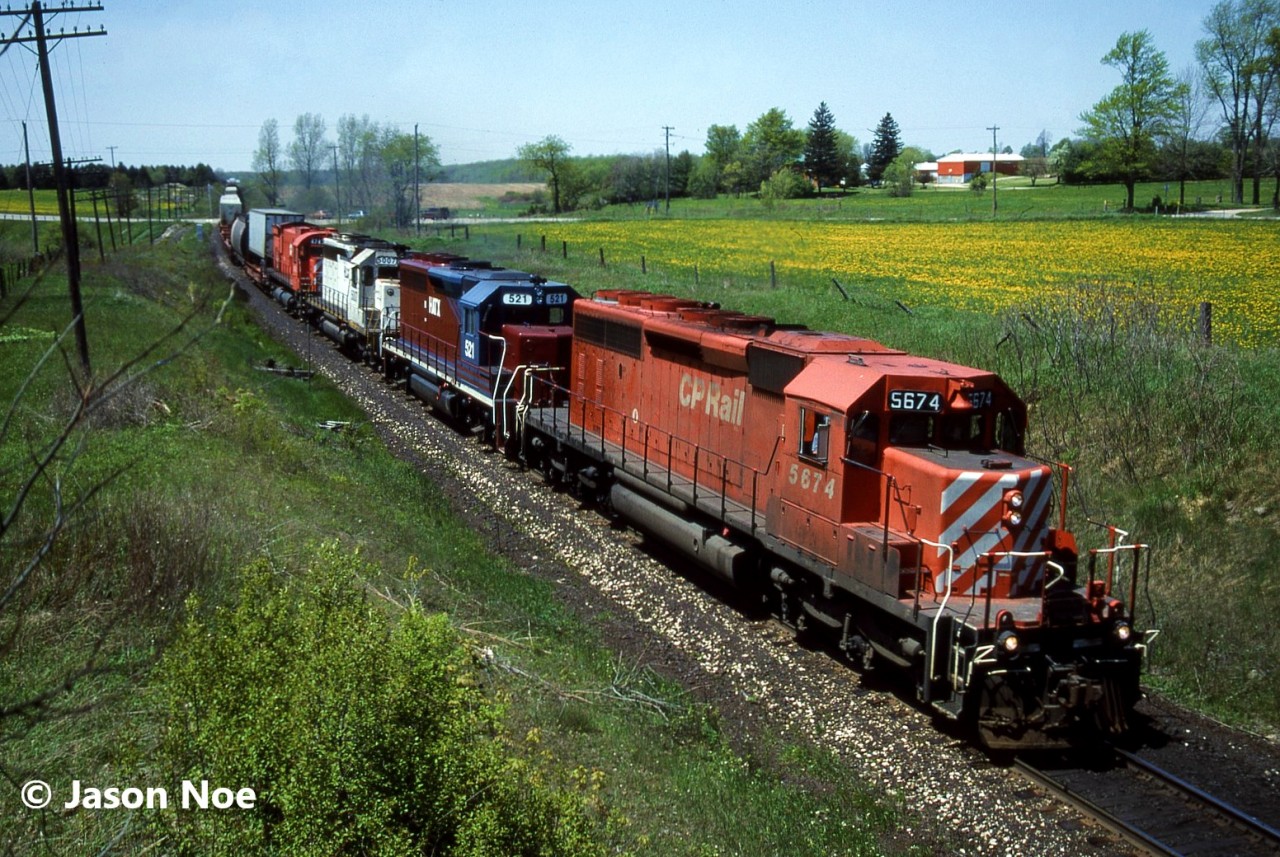 CP SD40-2 5674 is pictured leading an eastbound train under the wooden bridge near the Highway #2 crossing, just west of Woodstock, Ontario on the Galt Subdivision. The crew had just met train 511 with 5909 west at Zorra and was continuing east with work ahead at Woodstock and Guelph Jct. The consist included; HATX GP40 521, HLCX SD40 5007 and M-636 4743. The big MLW was eventually retired a few months later on August 28 and was sold to the Delaware-Lackawanna Railroad in 1997.