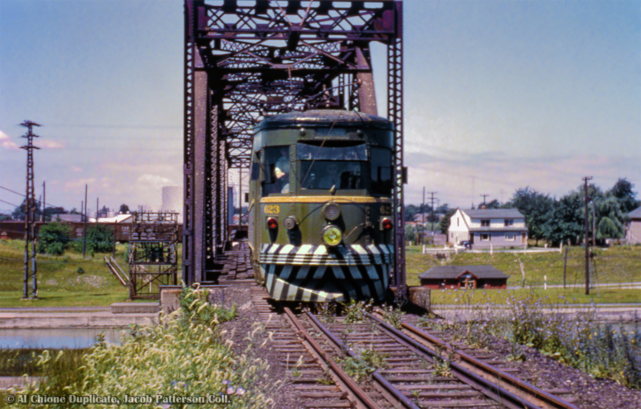Making its way down the former mainline to Niagara Falls, car 623 of the Niagara St. Catharine's & Toronto Railway is seen eastbound crossing bridge 8 over the Welland Canal on an excursion.  By 1948, this section of track became freight only to serve Walker's Quarry, about 1.5 miles north of this spot on the east side of the canal, though NS&T excursions were known to explore all the industrial spurs with the visiting railfans.  Built in 1930 by the Ottawa Car Company, 623 was the last of four cars built for the Windsor, Essex & Lake Shore Rapid Railway.  These were sold to the Montreal & Southern Counties Railway during the mid-1930s.  Of the four cars, 620, 622, and 623 would be transferred to the NS&T during the summer of 1955.  All three cars would be scrapped in 1959.   NS&T's mainline from St. Catharines - Niagara Falls began service in July 1900 via Merritton and Thorold, seeing passenger and freight movements.  Interchange was available with the CNR at both these intermediate locations, and with both the CNR and Wabash at Stamford on the CNR Welland Sub (today's Stamford Sub.)  Passenger service was first cancelled in June 1941, but revived during April the following year due to wartime measures.  The permanent end came during September 1947, with freight service wrapping up by the end of the year.  Rails would be lifted from Shriner's siding, just west of the canal, to Niagara Falls during the spring of 1948.   Canal bridge 8, built in 1915, but without ships passing through until 1930, would see its last electric movements in July 1960, and last rail movement in 1964.  At this time, two sidings were built for Walker's quarry off the south side of the Grimsby Sub, just west of the Taylor Road overpass.  Both sidings followed along the 1870s Grand Trunk Railway alignment, which curved south, passing beneath the third Welland Canal via a tunnel.  In the distance at left, boxcars can be seen on the NS&T-CNR interchange tracks, later becoming part of CN's Fonthill Spur, (1) used in recent years by GIO (2) and Trillium for car storage and access to Thorold customers.  CN's connection to this interchange was via the Thorold Sub, running from Merritton to Port Robinson.   Off to the right and below the NS&T tracks sits CN's Thorold station, built circa 1930 with the construction of the fourth Welland Canal.  Built as the Welland Railway from Port Colborne - Thorold circa 1859, and coming under Grand Trunk ownership during the early 1880s, the line ran parallel to the canal for most of its route, climbing the Niagara Escarpment initially as competition for the canal's traffic.  In the CNR era, this was the mainline for Fort Erie-bound trains, with Merritton - Thorold being helper territory.  Consolidations and Mikados, double and triple heading with Northerns, lifting freights upgrade, cutting off near the Thorold station.  Fort Erie racetrack trains from Toronto were also frequent visitors to this territory.  CN's Thorold station, shot by Arnold in 1976, would burn down during the late 1970s.   After the removal of canal bridge 10 in the late 1990s, what remained of the Thorold Sub was turned over to the Trillium Railway along with much of the Niagara industrial lines, which are presently in the hands of GIO Rail.  As of this writing, GIO stopped service over the Thorold Sub as of March 1, 2024, but the rails remain in place.   Aerial maps of the Niagara region can be viewed for each decade from the 1920s through the 1970s by clicking here.  Note various stages of canal construction (4th canal during the 1920s, and the Welland bypass project in the 1970s,) as well as railway relocations through the years.  The book, Niagara, St. Catharines & Toronto Railway by John M. Mills is also an excellent resource.   More Bridge 10: Mooney; 1997 Mooney; 1997  More Lock 7: Brown; 1997 Brown; 1998 Elliott; 2001 Host; 2021    Original Photographer Unknown, Al Chione Duplicate, Jacob Patterson Collection Slide.