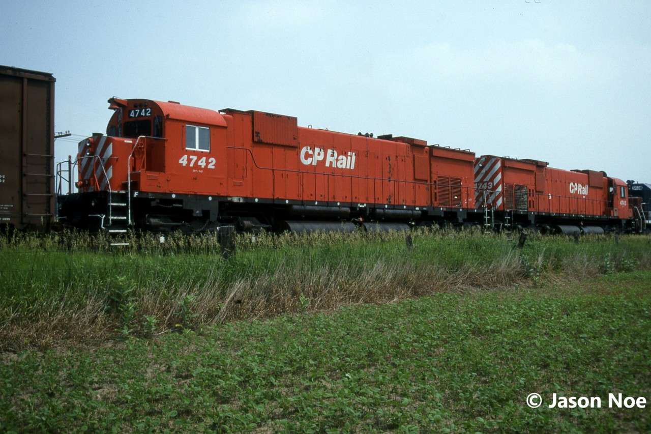 Amid an early summer heat wave, the Southern Ontario air sat heavy and muggy. In retrospect it was the beginning of a long dry season that would see many weeks with the same weather pattern. However, when you’re young these things tend to bother you less. Such was the case here as Andy Gertz and I headed towards London following the Galt Subdivision, in his compact orange Toyota. Once near the village of Ayr, his scanner crackled to life with the RTC calling 5527 east. The approaching eastbound was given a clearance to take the siding at nearby Wolverton for a meet with westbound intermodal 503. Being very close already, we diverted our route towards the east switch Wolverton to await both trains. At the time, Trussler Road was a much less busy thoroughfare and Wolverton was only a long siding in the middle of two farm fields, as the current Wolverton Yard was more than a decade away from being constructed. Soon 5527’s headlight came into view at the top of the siding’s crest, and the train slowly made its way towards us. In true mid-90’s fashion we had no idea what the power was, however with CP’s ever growing lease fleet odds were good it was going to be colourful. As 5527 neared we heard the unmistakable bark of not one but two M-636’s trailing, CP 4742 and 4743, behind the lead SD40 and HLCX 5008. 

In the final summer of their existence on CP, anytime you would see a big MLW could be your last, as by June 1995 only about 8 remained in service. And with CP’s new order of GE AC4400CW’s due to arrive in late summer the clock was ticking. So, on that muggy afternoon, Andy and I took many frames on Kodachrome of the two M-636’s as they waited the arrival of 503. Despite their impending retirements, both units still looked sharp in their matching action red paint, unlike many of the already fallen and retired M-636’s in the same class. With 503’s horn approaching from the east, we walked back to the crossing hoping 4742 and 4743 would put on a good show departing the siding following the meet….