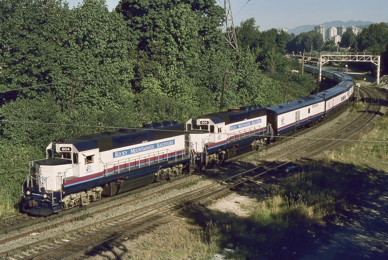 For their first few seasons, Rocky Mountaineer utilized ex ATSF GE B36-7 units, but in 1996, leased HELM GP40-3 power took over.  Here are HATX 804 and 805 eastward from Vancouver (timetable southward) on BNSF between signal gantries at Braid in New Westminster, and directly alongside the switch that provides the CP Jct. connection from CP’s Westminster sub., as seen on Thursday 1996-08-01 at 0851 PDT from the Brunette Avenue overpass.