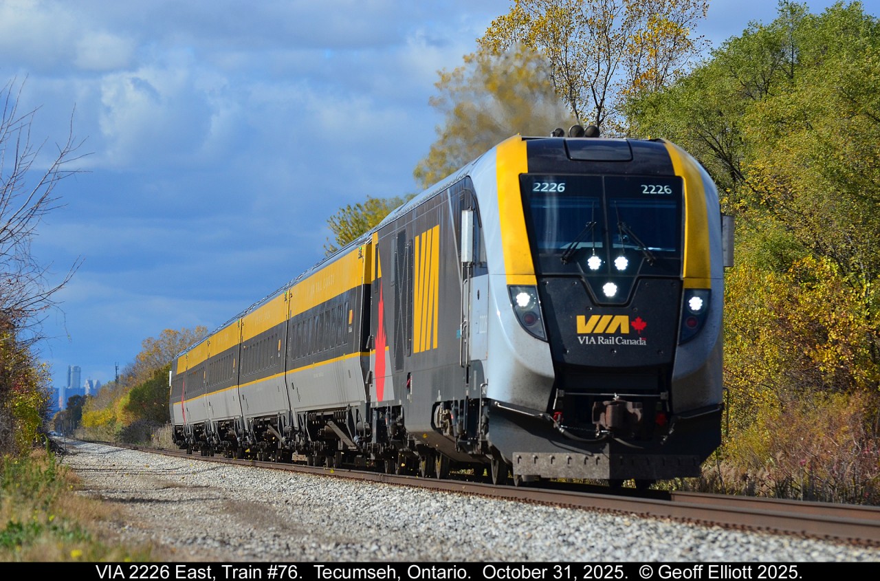 With the Detroit Renaissance Center looming in the background, VIA Charger #2229 leads eastbound VIA Train #76 out of Tecumseh, Ontario on October 31, 2025. With a mix of cloud and sun in the sky, and with about 1 minute to spare, the sun popped out to light up the shot and the little bit of Fall color that is still hanging around in the area.