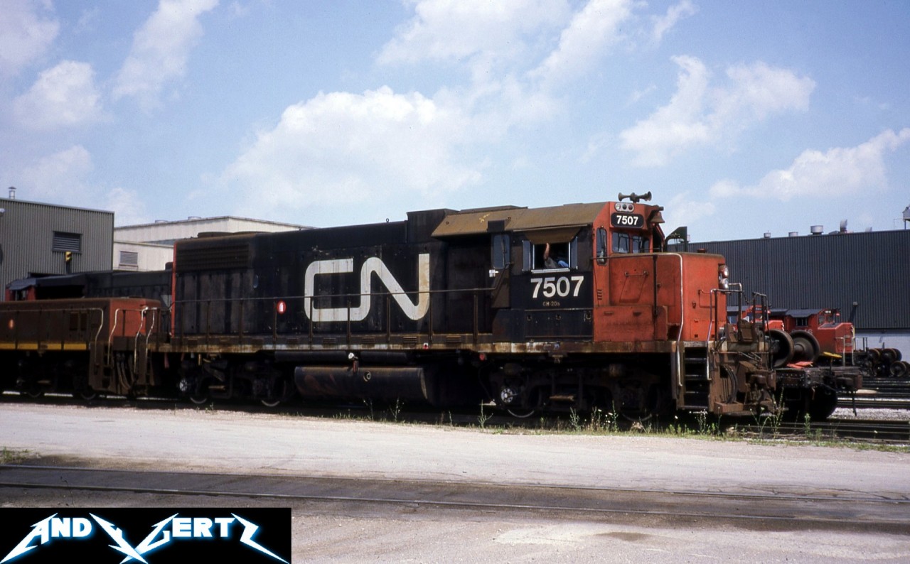 During a summer afternoon in 1987, shop crews are preparing to move GP38-2 7507 (former CN 5555) and its slug mate from the CN MacMillan Yard diesel shop in Vaughan, Ontario. Other power is seen in the background around the shop awaiting attention.