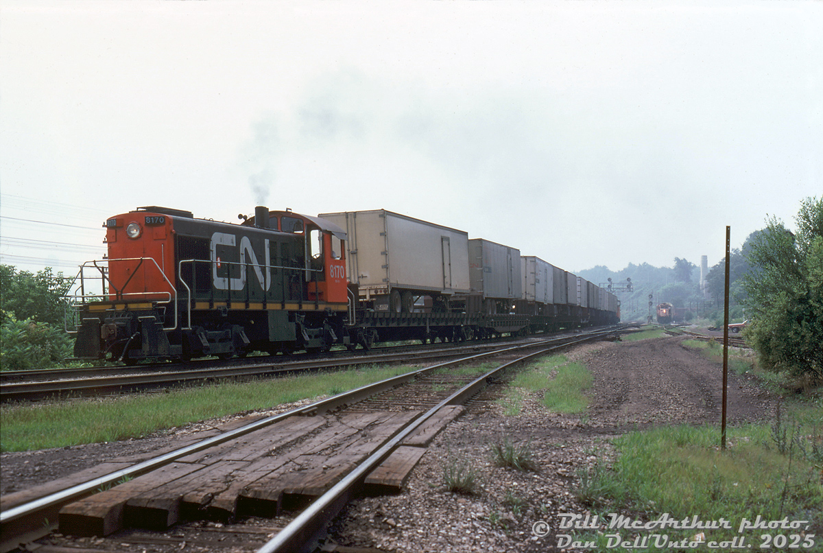 Hamilton-assigned CN S4 8170 handles a cut of loaded piggyback flatcars and caboose, heading eastbound through Hamilton Junction towards Bayview Junction on the Oakville Sub. The cowpath connecting track is visible in the foreground (Hamilton Jct-Hamilton West). This was noted by Bill as a "van turn" move, IIRC this was a yard job from nearby Stuart St. Yard sent out to wye the piggyback flats so the trailers/vans would be facing the correct way for "circus-unloading" (i.e. backing a truck over the cars to hook up and unload each trailer separately) at the piggyback ramp in the yard.

In the background on CP trackage is CP GP35 5002 and RS18 8788 handling a dimensional train with Ontario Hydro schnabel car HEPX 200, waiting to head up the Goderich Sub.

Bill McArthur photo, Dan Dell'Unto collection slide.