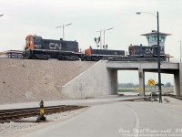 Clean ballast, fresh concrete, and newly converted hump power are all present in this view inside CN's Toronto Yard, their new state-of-the-art freight classification yard opened north of the city on 1000 acres of former Vaughan Township farmland. CN S13's 8607 and 8624 bracket slug B3 as they glide over the crest of the dual hump, past the North Switchtender's Tower, hump signals and access roads below. The original hump power, the 8600-series MLW S13's weighed more than the standard 8500-series units, were equipped with newer GE 752 traction motors, and were equipped with hump controls and some other features including the ability to power chopped-down slugs that were converted from retired MLW S3 switchers.<br><br>Bounded by the former hamlets of Edgeley, Concord, Maple and Sherwood, Toronto Yard was part of CN's "Toronto Bypass" project that diverted freight traffic north of the city via the new Halton and York Sub connections, and out of congested Toronto, thereby freeing up track time for GO Transit to start up commuter operations and take over part of CN's Mimico Yard for their own facilities (Willowbrook Yard). Renamed MacMillan Yard in 1975, it continues to serve an important part of CN's network today, albeit with newer technology and hump power. The S13-slug-S13 sets eventually gave way to GP38-2's and newer GMD-built slugs, and today SD40-2 variants and slugs.<br><br><i>Original photographer unknown, Dan Dell'Unto collection slide.</i> <br><br><u><i>More Toronto/MacMillan Yard photos:</i></u><br>C Yard tracks: <a href=http://www.railpictures.ca/?attachment_id=51354><b>http://www.railpictures.ca/?attachment_id=51354</b></a><br>Aerial view: <a href=http://www.railpictures.ca/?attachment_id=33864><b>http://www.railpictures.ca/?attachment_id=33864</b></a><br>South end: <a href=http://www.railpictures.ca/?attachment_id=52917><b>http://www.railpictures.ca/?attachment_id=52917</b></a><br>Departure/Arrival leads: <a href=http://www.railpictures.ca/?attachment_id=52621><b>http://www.railpictures.ca/?attachment_id=52621</b></a><br>Diesel Shop (outside): <a href=http://www.railpictures.ca/?attachment_id=1670><b>http://www.railpictures.ca/?attachment_id=1670</b></a><br>Diesel Shop (inside): <a href=http://www.railpictures.ca/?attachment_id=20758><b>http://www.railpictures.ca/?attachment_id=20758</b></a>