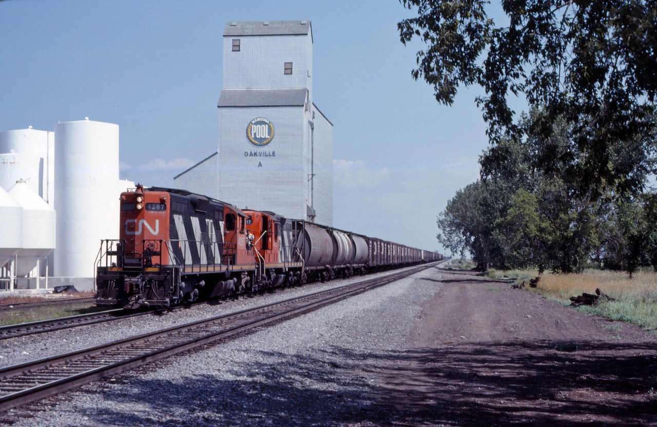A grain peddler heads west through Oakville, Manitoba behind "lightweight" GP9s 4287 and 4317 with a train of mostly 40 foot grain boxes. For a more current view of this location, see Darcy Woodhall's photo https://www.railpictures.ca/?attachment_id=57562