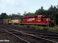 On a weekend summer day, a CP eastbound train is viewed lifting three boxcars from the CN interchange that connected to the CP St. Thomas Subdivision in Woodstock, Ontario. Previously, the power that included SD40-2 5664 and HLCX SD40 3087 had arrived from London, uncoupled from their train and went light down the St. Thomas Subdivision to the interchange. One would assume the three boxcars were fairly “hot” priority cars that couldn’t wait until Monday for one of the Woodstock jobs to lift. The tracks in the foreground are the CN Dundas Subdivision and today this location is known as Carew, however the interchange track between the two railways is long gone. 
