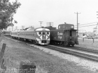 Having come up the Don Branch from Toronto Union Station and taken a right at Leaside, a pair of CP RDC-1's lead by 9060 head eastbound on the Belleville Sub at Mile 200, approaching the Birchmount Road grade crossing and the Highway 401 underpass. They're passing the tail end of a westbound CP freight that appears to have a good amount of stock cars on the rear, with CP steel offset-cupola caboose 437399 bringing up the markers. On the right is Canron Ltd's pipe manufacturing facility in Scarborough (served by rail siding), that became the site of a Simpsons-Sears warehouse in the early 1970's.<br><br><i>Original photographer unknown (possibly a Bill Grandin photo), Dan Dell'Unto print collection.</i>