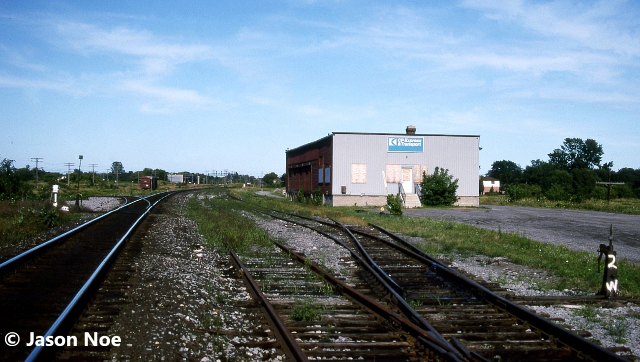 During the mid-90’s, Cobourg, Ontario’s long closed Canadian Pacific Express & Transport regional freight warehouse building still stood as part of the railway scene situated along the Belleville Subdivision almost frozen in time. It was located across from the interchange tracks with CN’s parallel Kingston Subdivision where the lone boxcar is pictured. Eventually it was slated for demolition by CP, however in 1996, it was purchased by a company named Legacy. Over time, they fully repaired and revived the neglected building and adjoining property into a thriving building materials and antique collectables business. Today it serves as Legacy Vintage’s warehouse, while the small yard beside the original CP express building has since been removed.