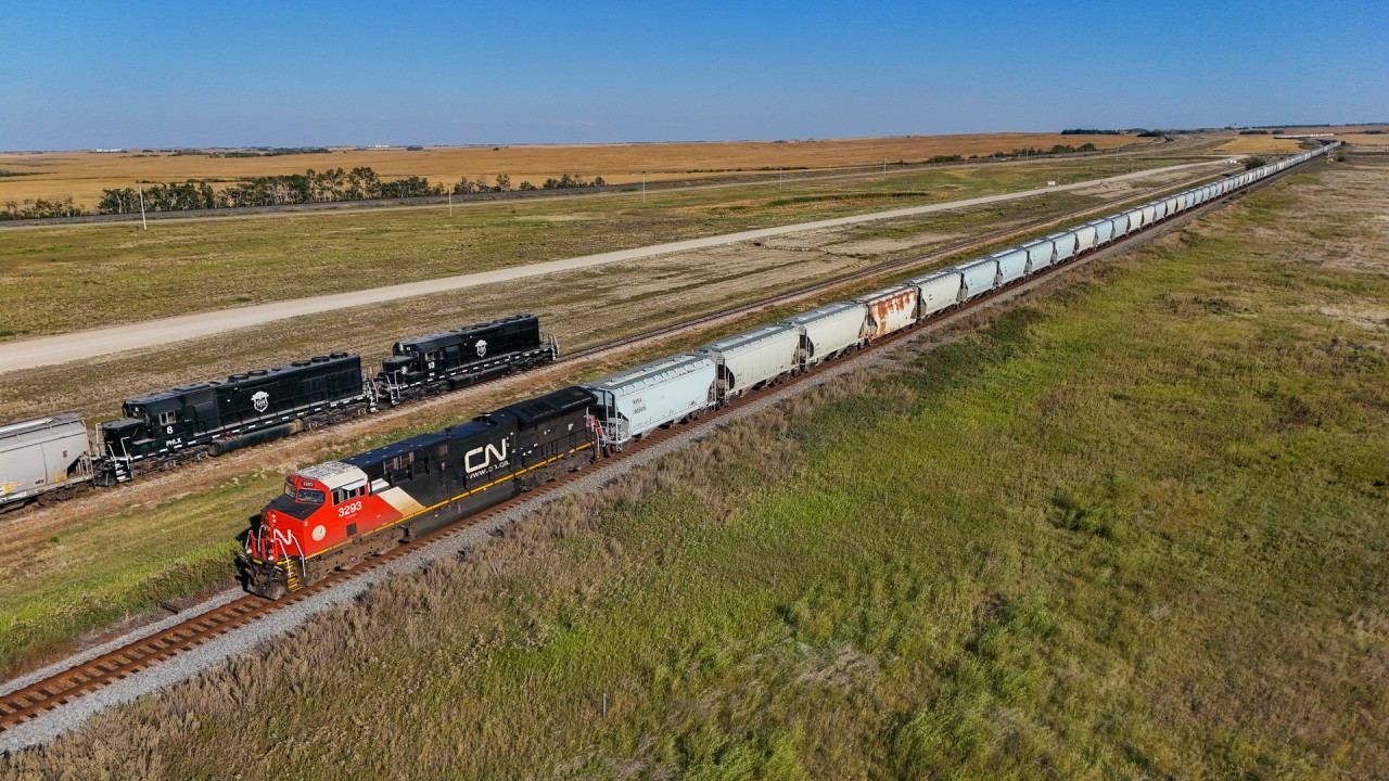 Harvest season is upon us.  A pair of Parish and Heimbecker units creep along the elevator track at Oban, slowly loading grain for export on the west coast. On the mainline, S 77581 13 races by with a 203 car frac sand train, bound for the oil fields of Western Canada, where “harvest season” runs year round.