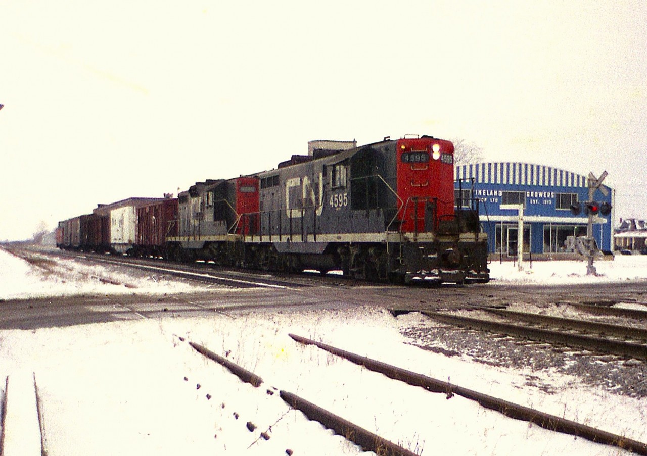 Typical blah winters-type day; grey terrain and grey skies and I am down at Jordan Rd crossing to see a local heading back to Niagara Falls (I presume) with an odd assortment of cars. I think this train had been working down at Winona, where the small yard there had a collection of rolling stock similar to what is on this train. CN GP9s are the power; 4595 and 4598. On the right is the old Vineland Growers Co-op building; current day this 100 year old business has a new sprawling building complex close by.