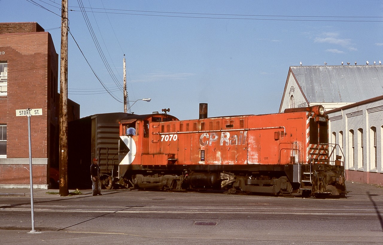 The CP E&N mainline ended at mile 0 at Store and Cormorant Streets in Victoria, but rails continued compass northward on Store Street to serve industrial customers and a freight shed and transloading yard.  A priority customer was Swift Canadian Company’s meat packing plant, frequently the first switch move for the Victoria 0600 yard crew.  On Monday 1979-04-23, their assigned unit was Baldwin DS4-4-1000 CP 7070, shown here spotting a mechanical refrigerator car to Swift’s, engineer Ken Barr.

Note the clear display of the unit number ahead of the cab, compared with the well-worn lettering on the hood side.  An often-applied theory of mine was that an engine deserves its number clearly displayed, done bit by bit on quiet graveyard shifts at the roundhouse.

CP 7070 is notable as the only one of CP’s eleven Baldwin switchers to never serve on Vancouver Island for the first 29 years of their existence since new in 1948.  By some happy coincidence, with most of the switchers out of service, 7070 survived to finally visit the E&N starting in January of 1978, and with 7072 lasted until April 1982.