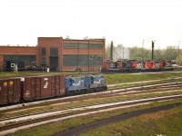 Conrail 5439 and 5441 are seen bringing over the daily transfer to Fort Erie. In behind is the once-busy CN shop complex. Lot of engines there, as usual, and at least five Geeps can be seen. Note on the left a shell of an unknown unit on a flat car. Some fairly heavy work was done in the shop as well.