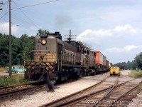Heading southbound on Canadian Pacific's MacTier Subdivision, CP RS2 8407 leads C424 4218 on a southbound freight on the mainline past the south siding switch at Bala, over the grade crossing at Gordon Street. The passing siding is full of maintenance of way equipment, including an errant speeder not quite on the rails. A short siding on the right branches off to Weismiller Lumber, with a boxcar spotted on it.
<br><br>
8407 was one of a small handful of RS2 units CP purchased (5 US-service units from Alco without MU, 4 from MLW with MU), and at the time one of only two in road service in Canada (later the only one, that was eventually demoted to yard service in St. Luc), so it was a rare shot to have 8407 leading a mainline freight. The irony is sister units 8405 and 8408 were traded in on C424's 4217 & 4219 (4218's trade-in unit was FB1 4402).
<br><br>
<i>Original photographer unknown, Dan Dell'Unto collection slide.</i>
<br><br>
----------------------
<br><br>
This unmarked slide was very difficult to identify the location of, and a story in itself. It came with some others from an unknown Toronto-area photographer in the late 60's/early 70's. The rarity of 8407 leading made it an instant buy, despite it having no location or other information noted. The codeline telegraph poles and signals suggested this was a mainline freight and not on a branchline, helping narrow things down. At first it looked like a freight along the Belleville Sub, and a few locations east of Toronto looked similar but no exact matches. Checking some old timetables, the telegraph line arrangements were listed and this one was most similar to the MacTier Sub, but there were no obvious locations that looked similar. The north end of Weston in Toronto had a vague similarity to this scene, but it also wasn't a match. Extra research included queries to the late Bruce Chapman and Ray Kennedy, but they were unfamiliar with the location. The slide was scanned but filed back with no idea where it was taken.
<br><br>
Further digging one day a year or two later lead to the north end of the MacTier Sub, and a search of all the siding locations. A breakthrough came noticing there were similarities to the south end of the siding in Bala, but Google Earth had no street imagery for the crossing - but Apple Maps did, which is very much changed today but the topography still bore some similarities, including a remaining codeline pole. Looking for old track maps or aerial imagery to show the siding arrangement yielded no results, but checking an old 1921 CP MacTier Sub track profile on CPHA confirmed a very similar siding arrangement at the south end of Bala, with that offshoot siding branching off to Weismiller Lumber. Looks like the mystery was finally solved. A lot of research to track down the obscure location of one 55-year old slide.
<br><br>
---------------
<br><br>
Bala is also notable in that it had a separate "Summer Station" to the west by the harbour/wharf for tourists . CP would run daily summer (and later weekend only) trains north to the station for tourists to connect with the daily steamboats, and a "Winter Station" just NE of Gordon St. crossing (behind the power in the photo) for off-peak season use. This lasted until the early 60's (some sources say 1950's), when the summer station was demolished. It's unclear when CP demolished the remaining winter station.
