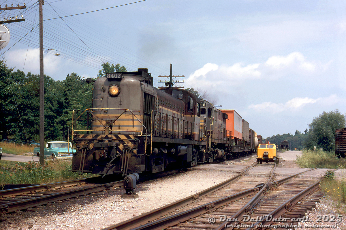 Heading southbound on Canadian Pacific's MacTier Subdivision, CP RS2 8407 leads C424 4218 on a southbound freight on the mainline past the south siding switch at Bala, over the grade crossing at Gordon Street. The passing siding is full of maintenance of way equipment, including an errant speeder not quite on the rails. A short siding on the right branches off to Weismiller Lumber, with a boxcar spotted on it.

8407 was one of a small handful of RS2 units CP purchased (5 US-service units from Alco without MU, 4 from MLW with MU), and at the time one of only two in road service in Canada (later the only one, that was eventually demoted to yard service in St. Luc), so it was a rare shot to have 8407 leading a mainline freight. The irony is sister units 8405 and 8408 were traded in on C424's 4217 & 4219 (4218's trade-in unit was FB1 4402).

Original photographer unknown, Dan Dell'Unto collection slide.

----------------------

This unmarked slide was very difficult to identify the location of, and a story in itself. It came with some others from an unknown Toronto-area photographer in the late 60's/early 70's. The rarity of 8407 leading made it an instant buy, despite it having no location or other information noted. The codeline telegraph poles and signals suggested this was a mainline freight and not on a branchline, helping narrow things down. At first it looked like a freight along the Belleville Sub, and a few locations east of Toronto looked similar but no exact matches. Checking some old timetables, the telegraph line arrangements were listed and this one was most similar to the MacTier Sub, but there were no obvious locations that looked similar. The north end of Weston in Toronto had a vague similarity to this scene, but it also wasn't a match. Extra research included queries to the late Bruce Chapman and Ray Kennedy, but they were unfamiliar with the location. The slide was scanned but filed back with no idea where it was taken.

Further digging one day a year or two later lead to the north end of the MacTier Sub, and a search of all the siding locations. A breakthrough came noticing there were similarities to the south end of the siding in Bala, but Google Earth had no street imagery for the crossing - but Apple Maps did, which is very much changed today but the topography still bore some similarities, including a remaining codeline pole. Looking for old track maps or aerial imagery to show the siding arrangement yielded no results, but checking an old 1921 CP MacTier Sub track profile on CPHA confirmed a very similar siding arrangement at the south end of Bala, with that offshoot siding branching off to Weismiller Lumber. Looks like the mystery was finally solved. A lot of research to track down the obscure location of one 55-year old slide.

---------------

Bala is also notable in that it had a separate "Summer Station" to the west by the harbour/wharf for tourists . CP would run daily summer (and later weekend only) trains north to the station for tourists to connect with the daily steamboats, and a "Winter Station" just NE of Gordon St. crossing (behind the power in the photo) for off-peak season use. This lasted until the early 60's (some sources say 1950's), when the summer station was demolished. It's unclear when CP demolished the remaining winter station.